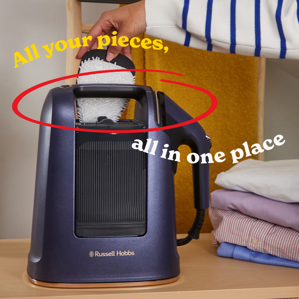 Egy személy egy tisztítópárnát helyez egy kék Russell Hobbs gőztisztítóba. Jobbra hajtogatott ingek vannak egymásra rakva.