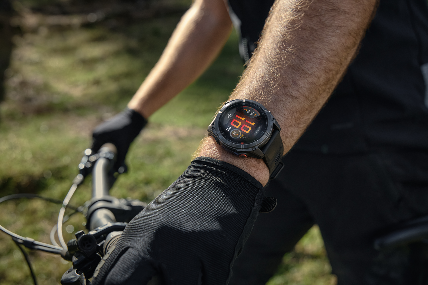 Una persona con un reloj negro en la muñeca mientras sostiene el manillar de una bicicleta. El reloj muestra la hora y otros datos.