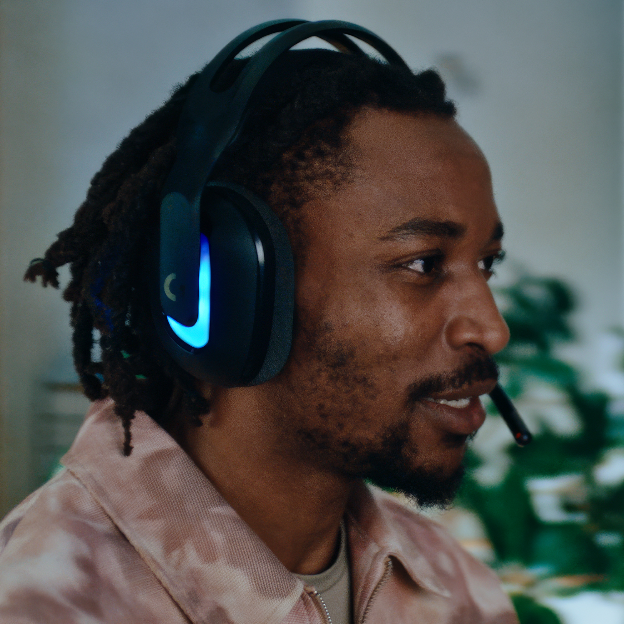 Mężczyzna w słuchawkach z mikrofonem. Ma dredy i różową koszulę. Słuchawki mają niebieskie światła.