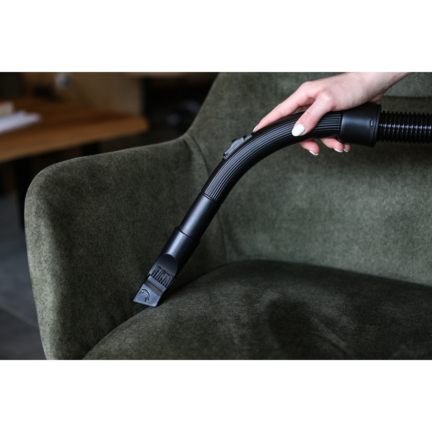 Una mano usa un accessorio nero per aspirapolvere su una poltrona verde. L'ugello tocca il tessuto.