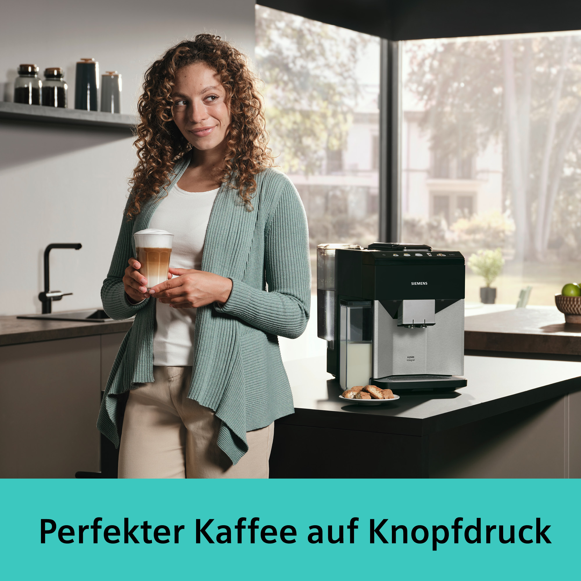 Eine Frau hält ein Kaffeegetränk neben einer Kaffeemaschine. Die Szene spielt in einer modernen Küche.