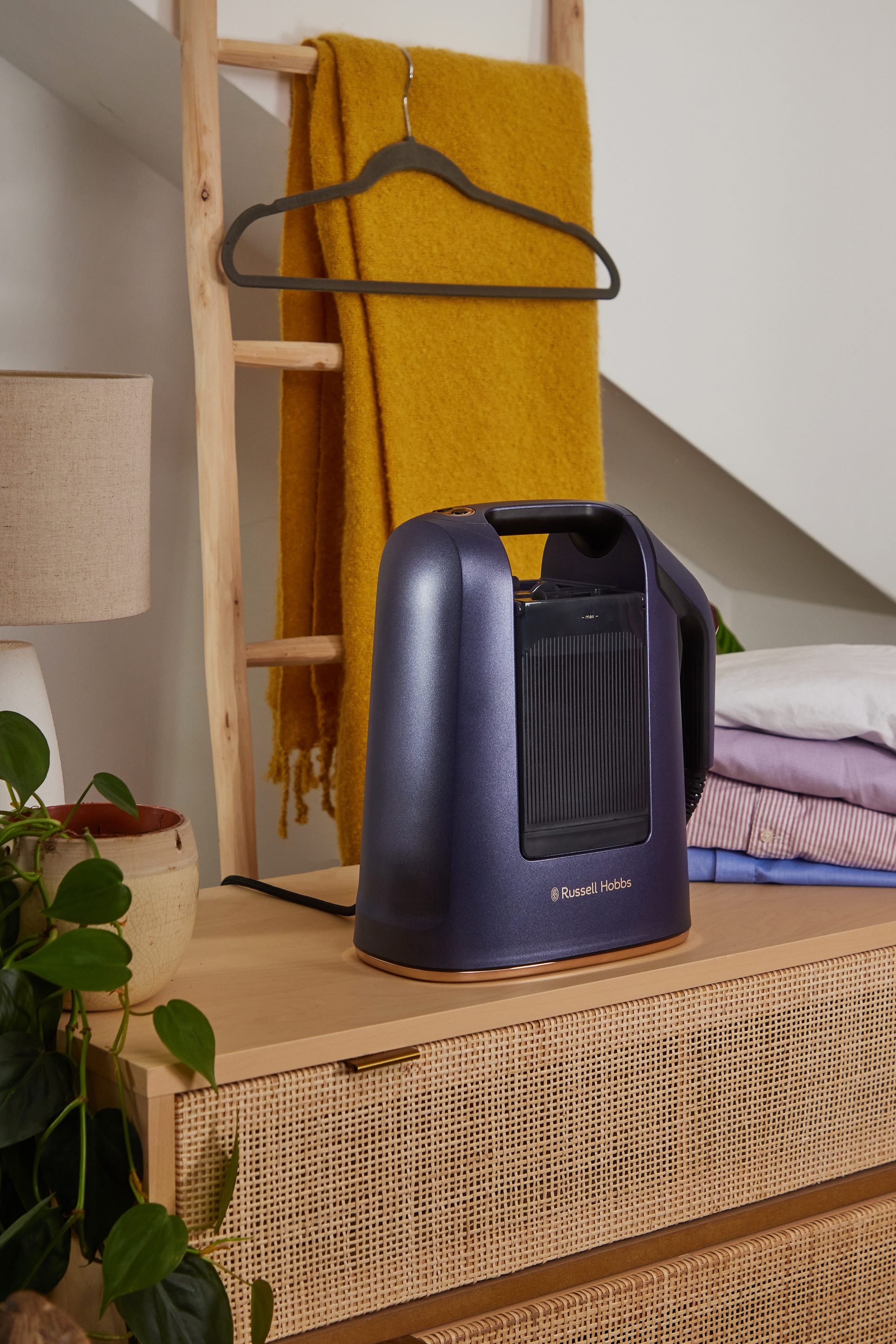 Egy kék Russell Hobbs gőzölő egy fa felületen. Egy sárga takaró lóg egy létrán a háttérben.