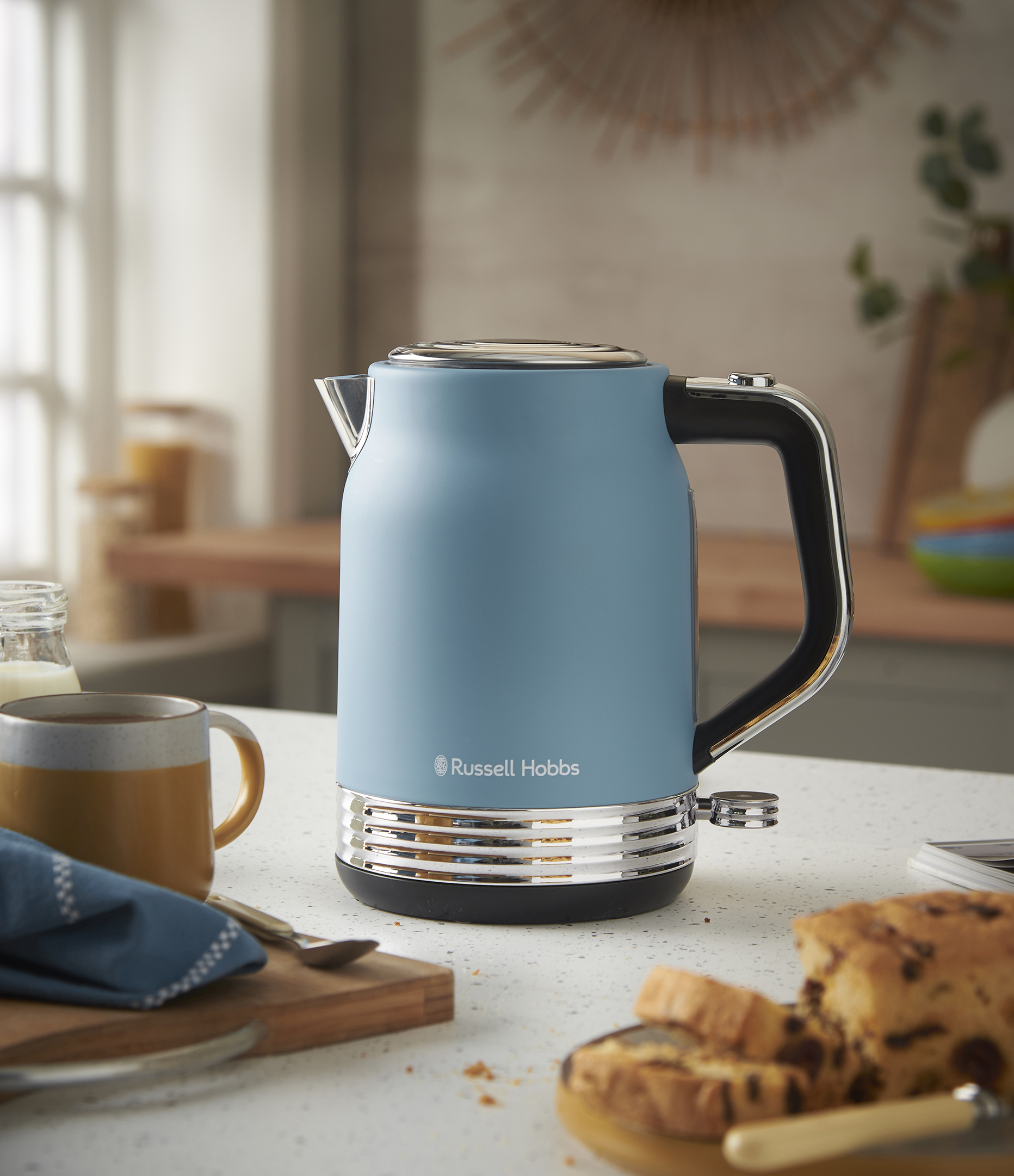 Kék Russell Hobbs vízforraló a pulton. Egy bögre, kenyér és egy üveg is a pulton található.