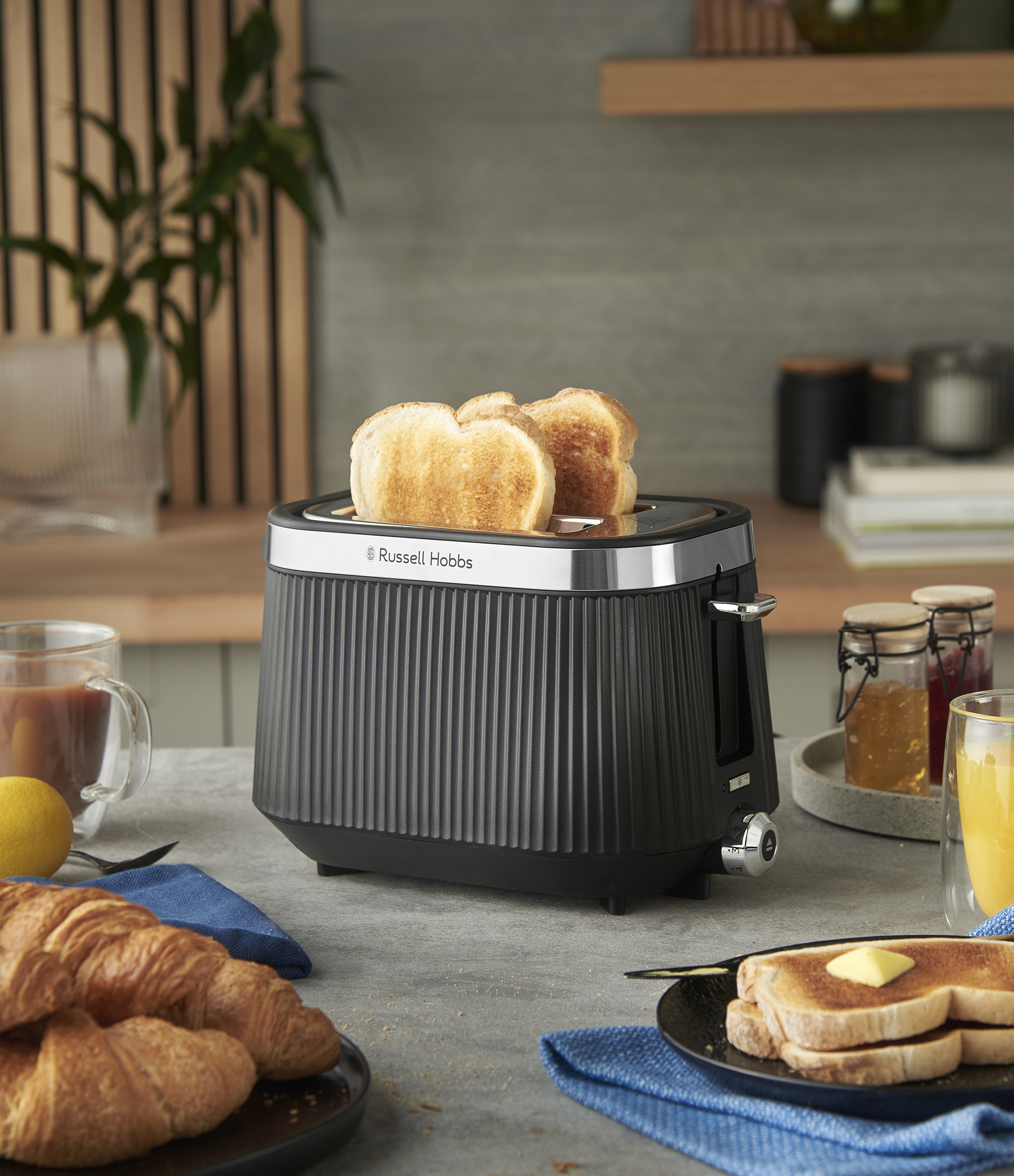 Pirítós kenyérrel, croissant-okkal és vajjal megkent pirítóssal teli kenyérpirító egy asztalon itallal és lével.