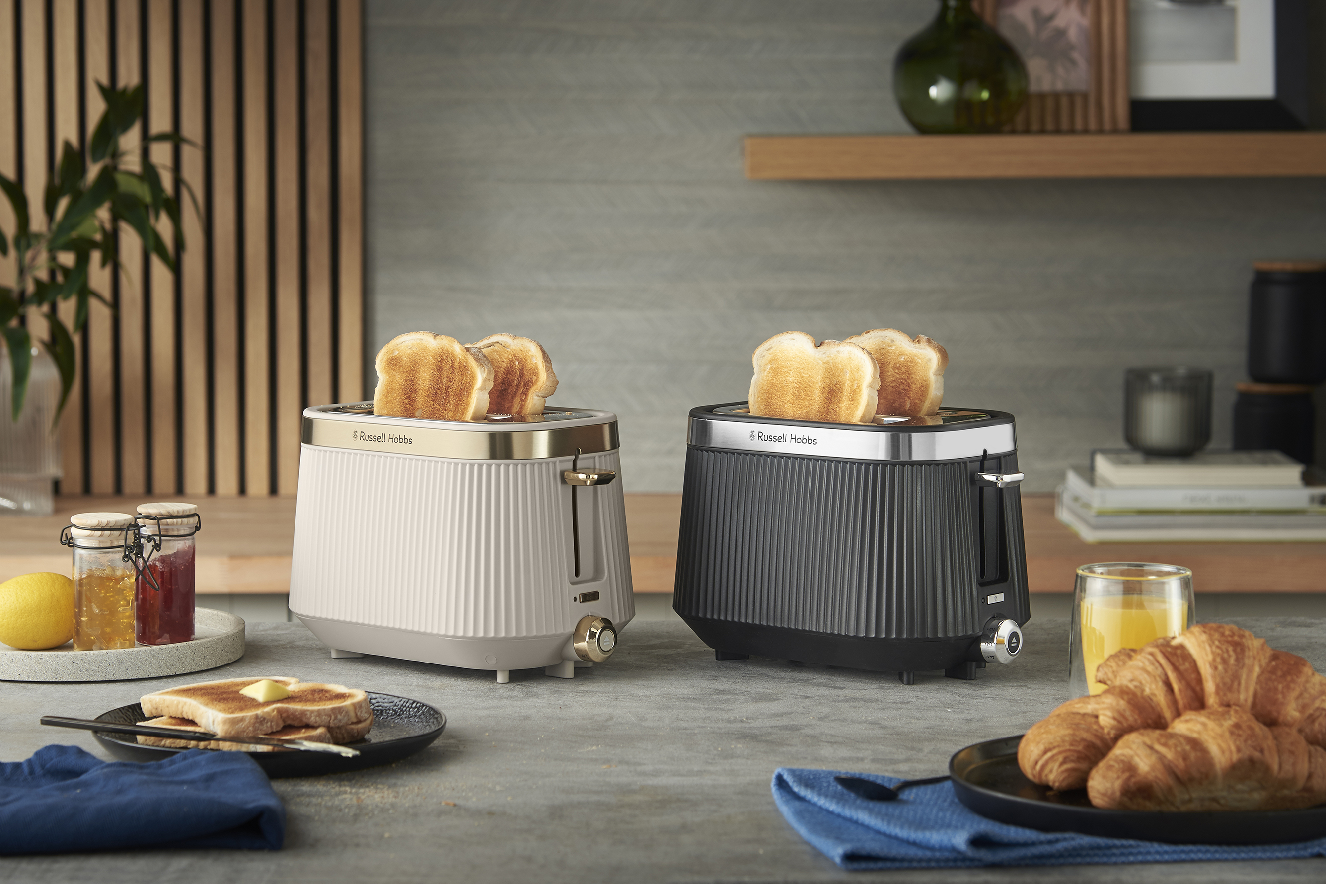 Két kenyérpirító pirítóssal. Egy asztal pirítóssal, vajjal, lekvárral, citrommal, croissant-nal és lével.