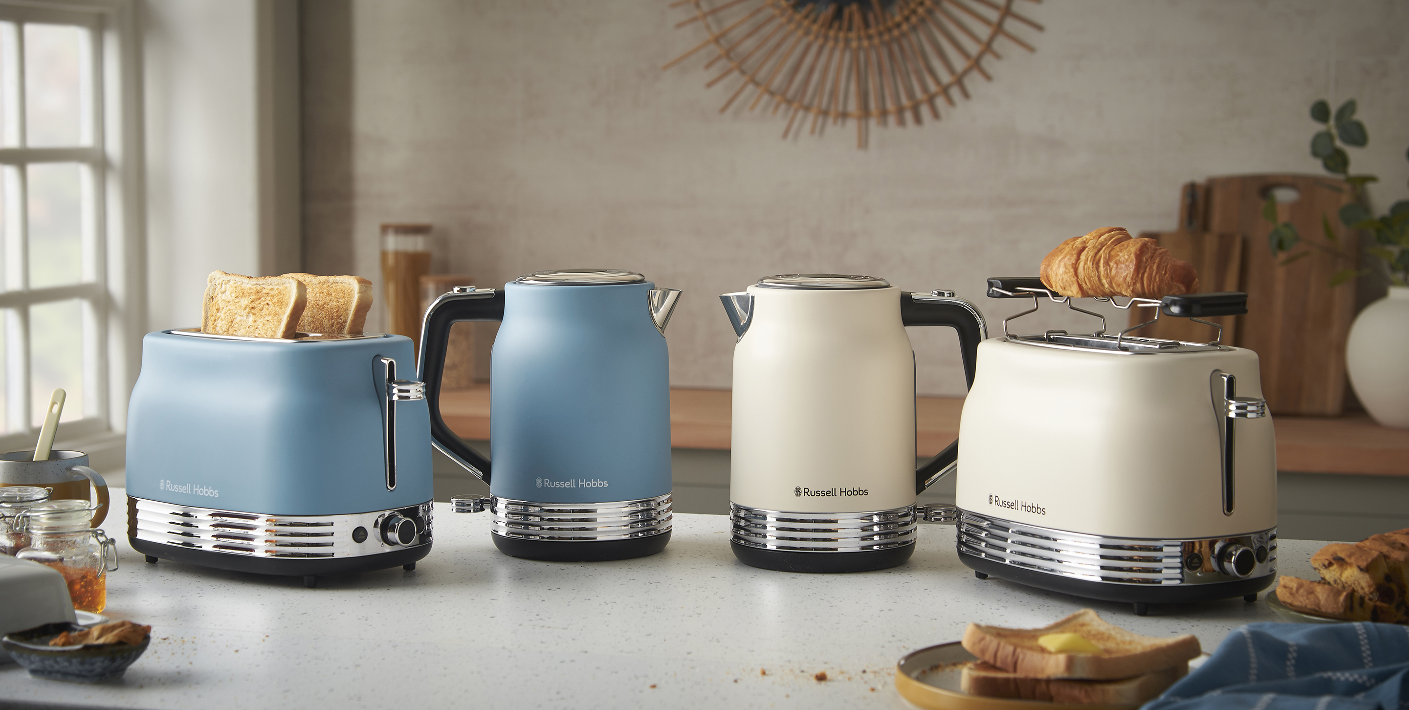 Kék és krémszínű Russell Hobbs készülékek. Kenyérpirítók kenyérrel és croissant-nal. Vízforralók. Konyhapult reggeli elemekkel.