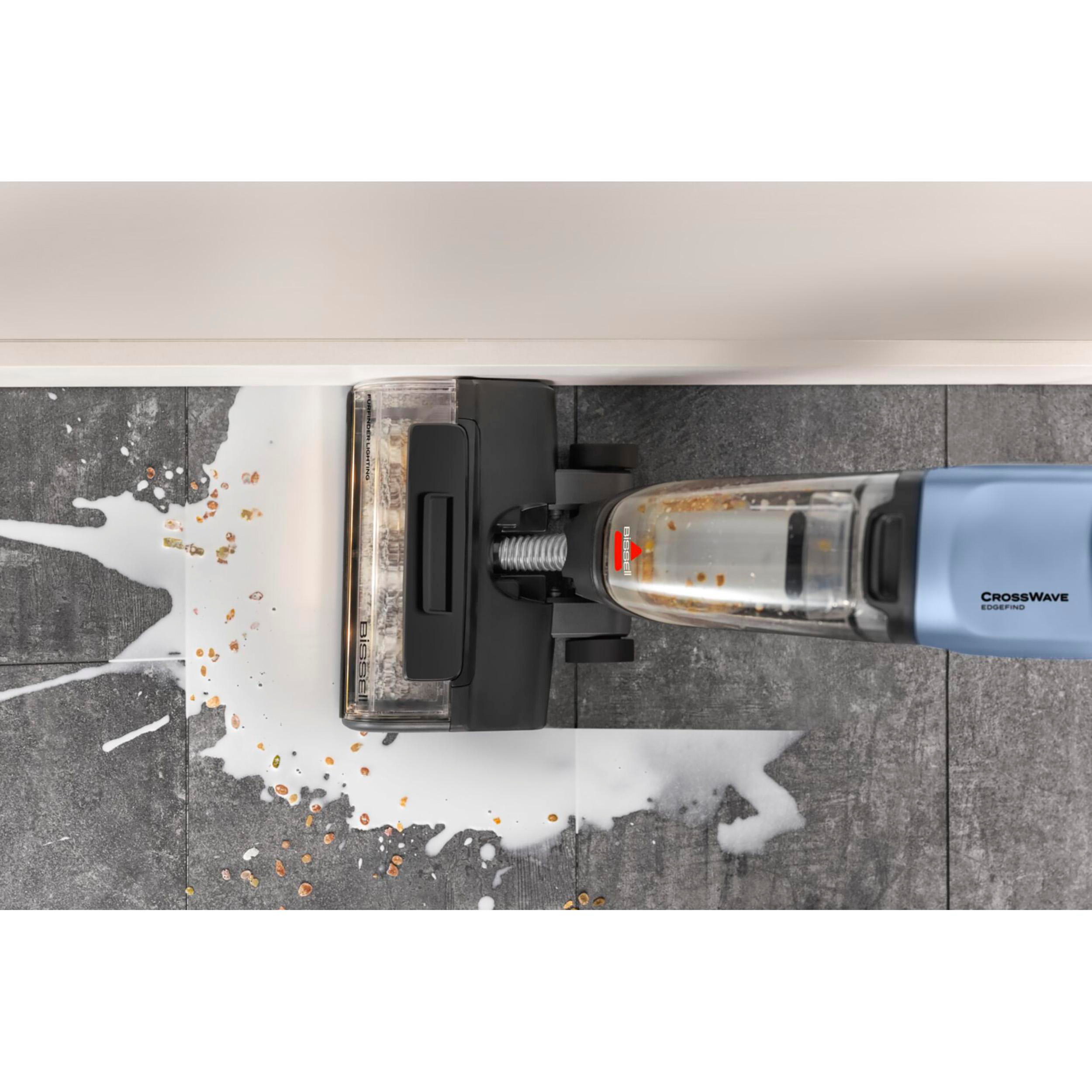 Ein Bissell CrossWave-Reiniger auf grau gefliestem Boden, der eine milchige Flüssigkeit mit Ablagerungen reinigt. Blauer Griff und weiße Wand.