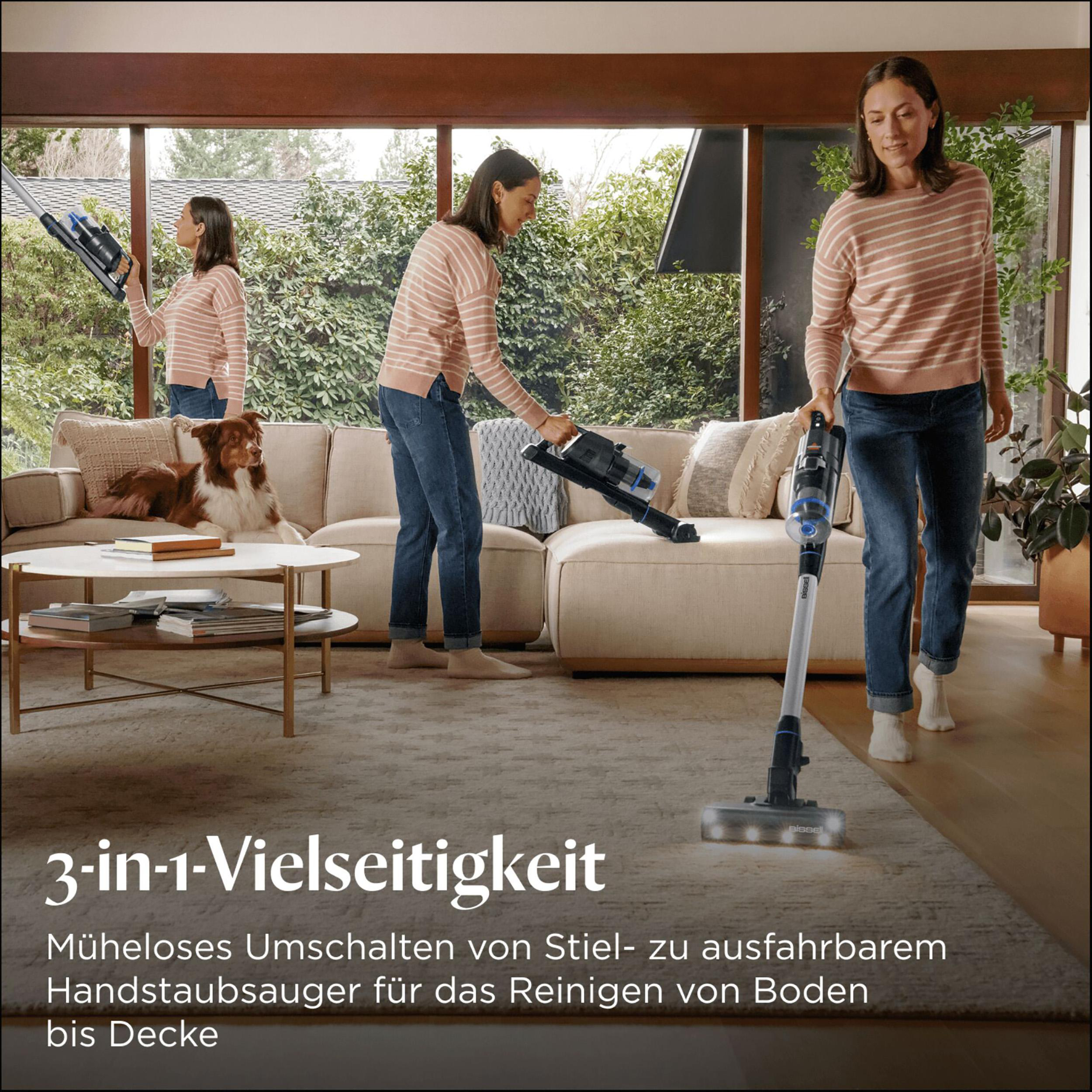Eine Frau saugt ein Wohnzimmer mit einem 3-in-1-Staubsauger. Auf dem Sofa liegt ein Hund, im Hintergrund eine weitere Frau.
