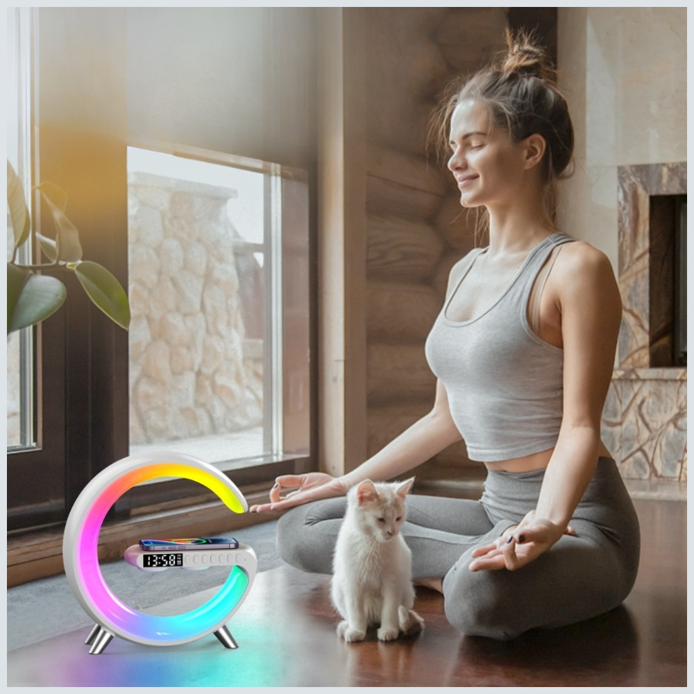 Kobieta medytuje obok kota, urządzenia z tęczowym oświetleniem i okna. Ma na sobie szary strój sportowy, oczy zamknięte.