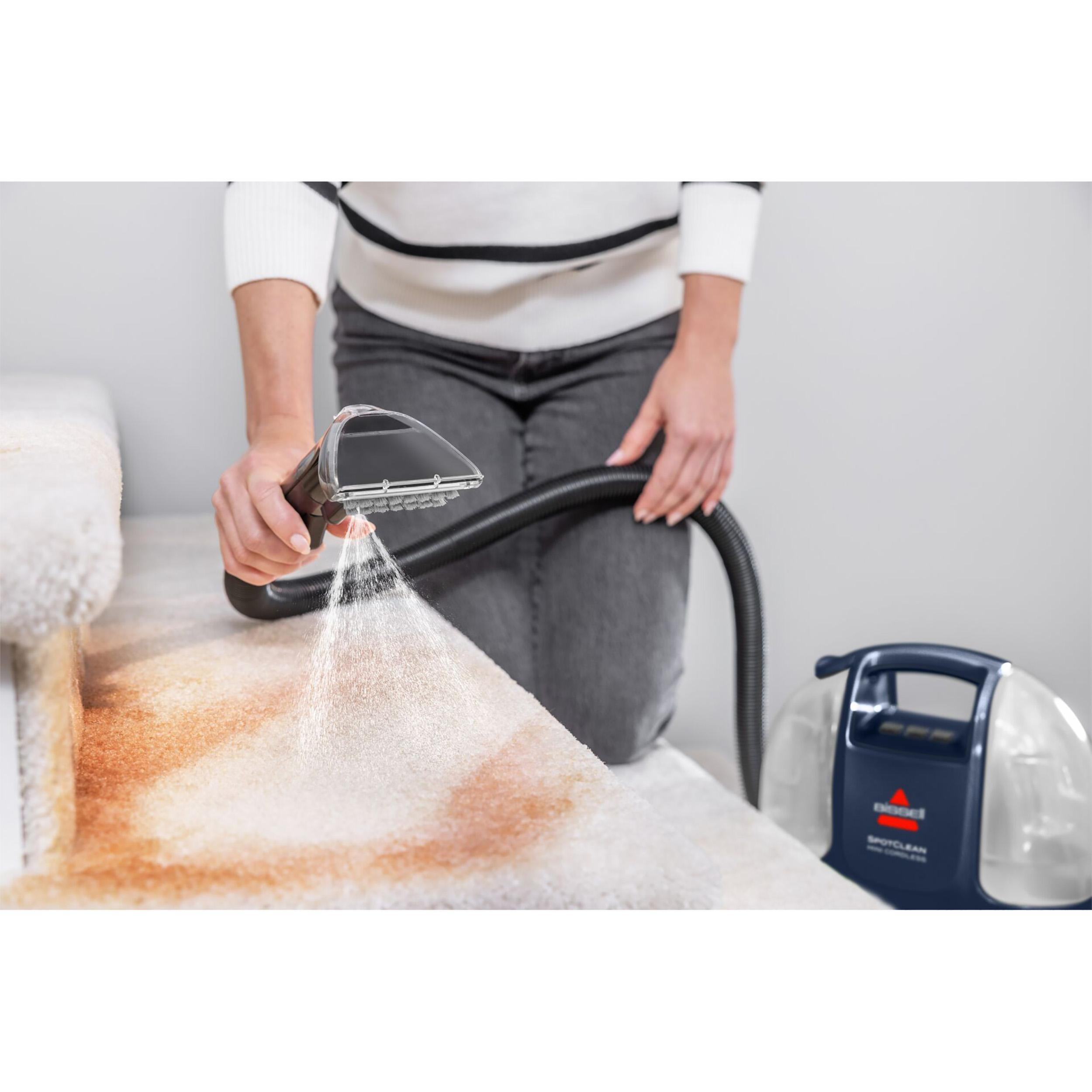 Person verwendet einen Bissell SpotClean, um eine befleckte Teppichtreppe zu reinigen. Maschine und Schlauch sind sichtbar.