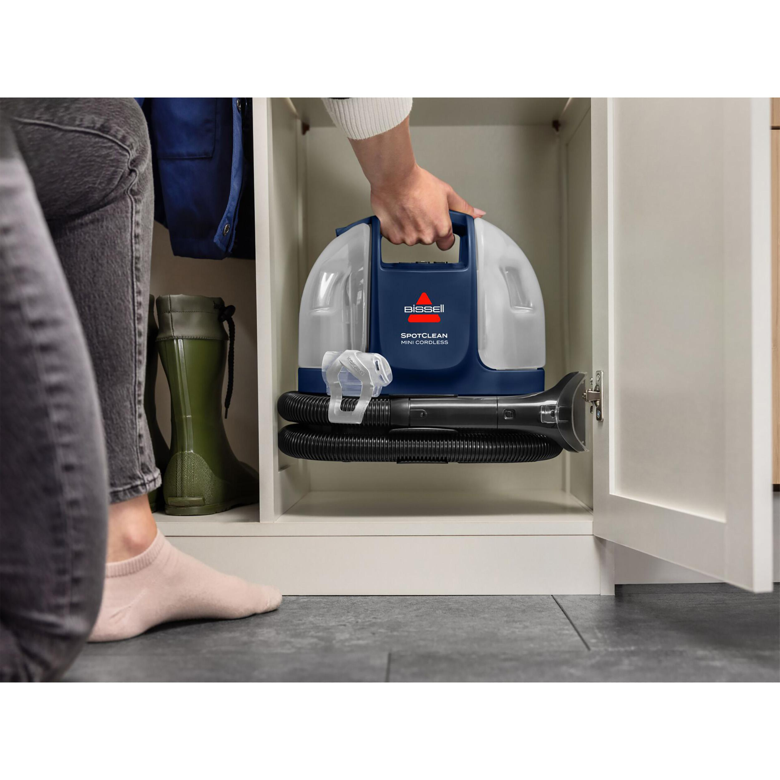 Eine Person hält einen blau-weißen Bissell SpotClean Mini-Akku-Staubsauger in einem weißen Schrank.