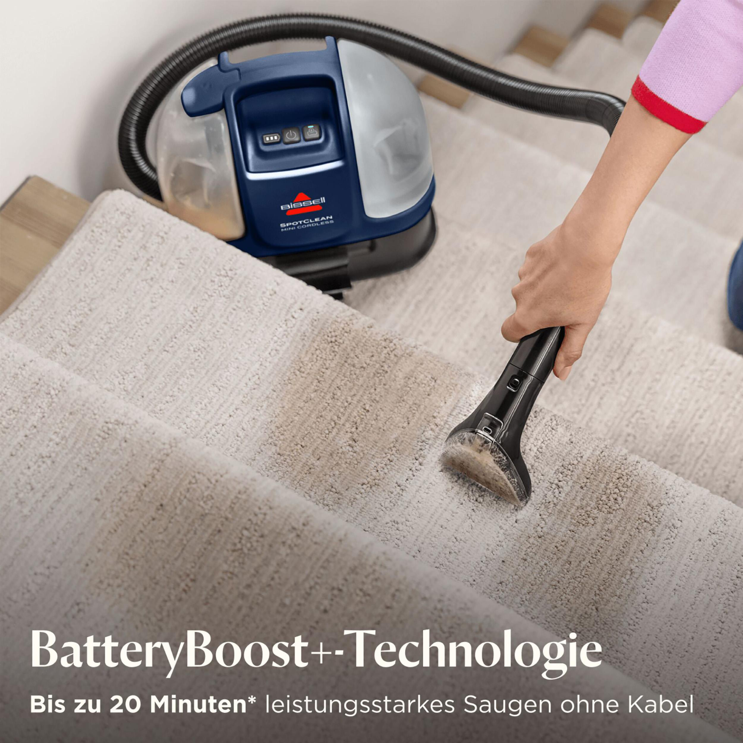 Eine Person, die einen Bissell SpotClean-Staubsauger auf einer beigefarbenen Teppichtreppe verwendet. Ein blauer Staubsauger ist sichtbar.