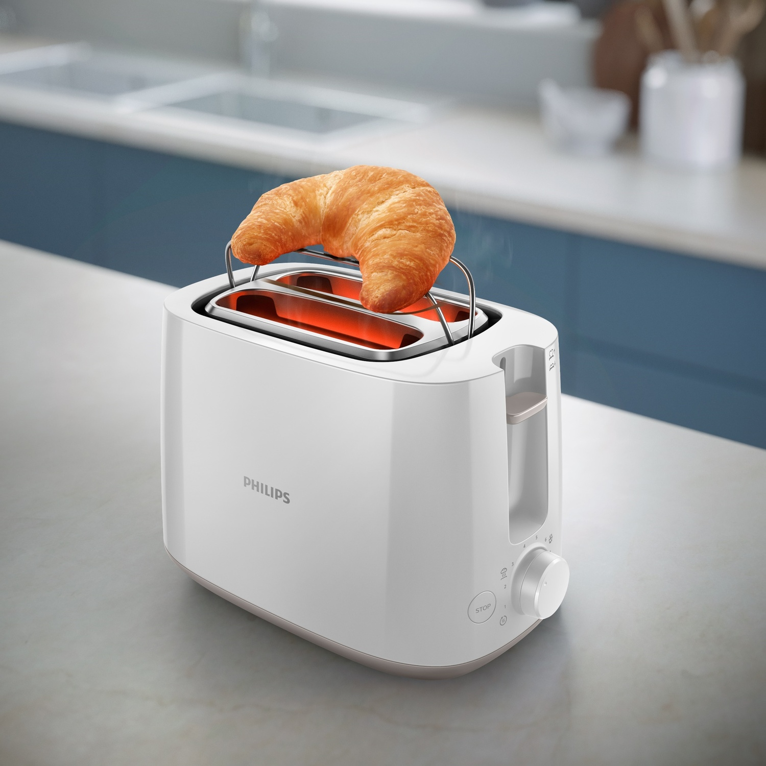 Un tostapane Philips bianco con un croissant sopra. Il tostapane è su un bancone con una cucina sullo sfondo.
