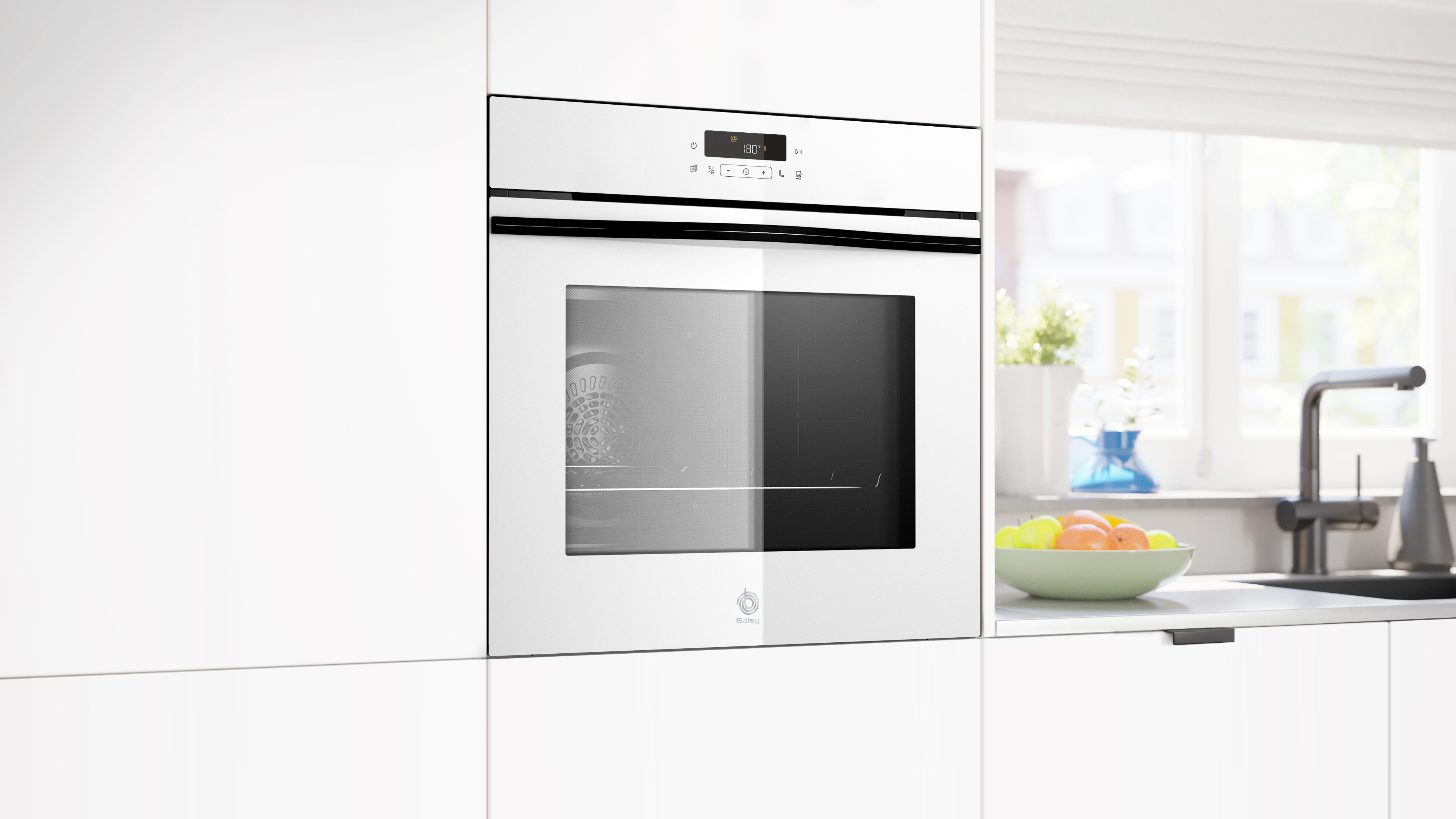 Un horno empotrado blanco con puerta de cristal, pantalla digital y frutero en una encimera junto a una ventana.