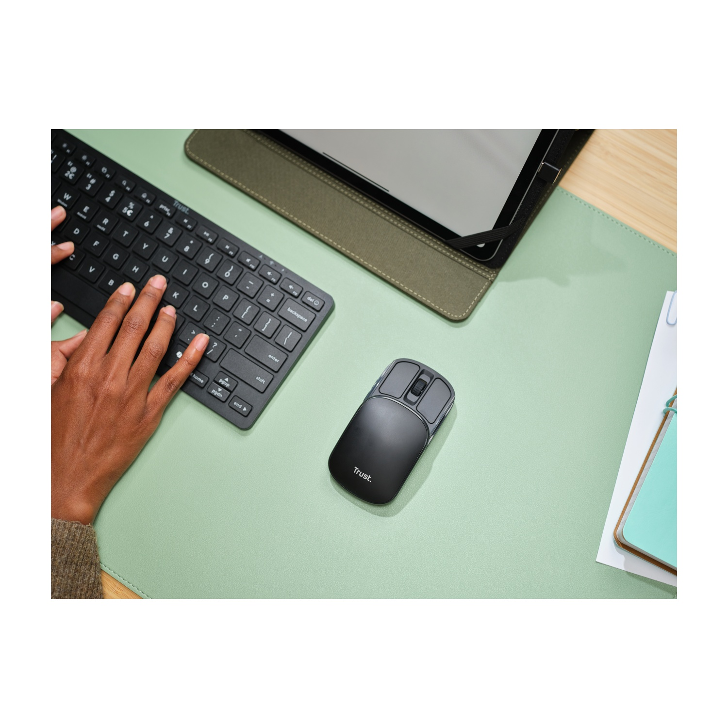 Mani che digitano su una tastiera nera su un tappetino verde. Sono visibili anche un mouse nero e un tablet.