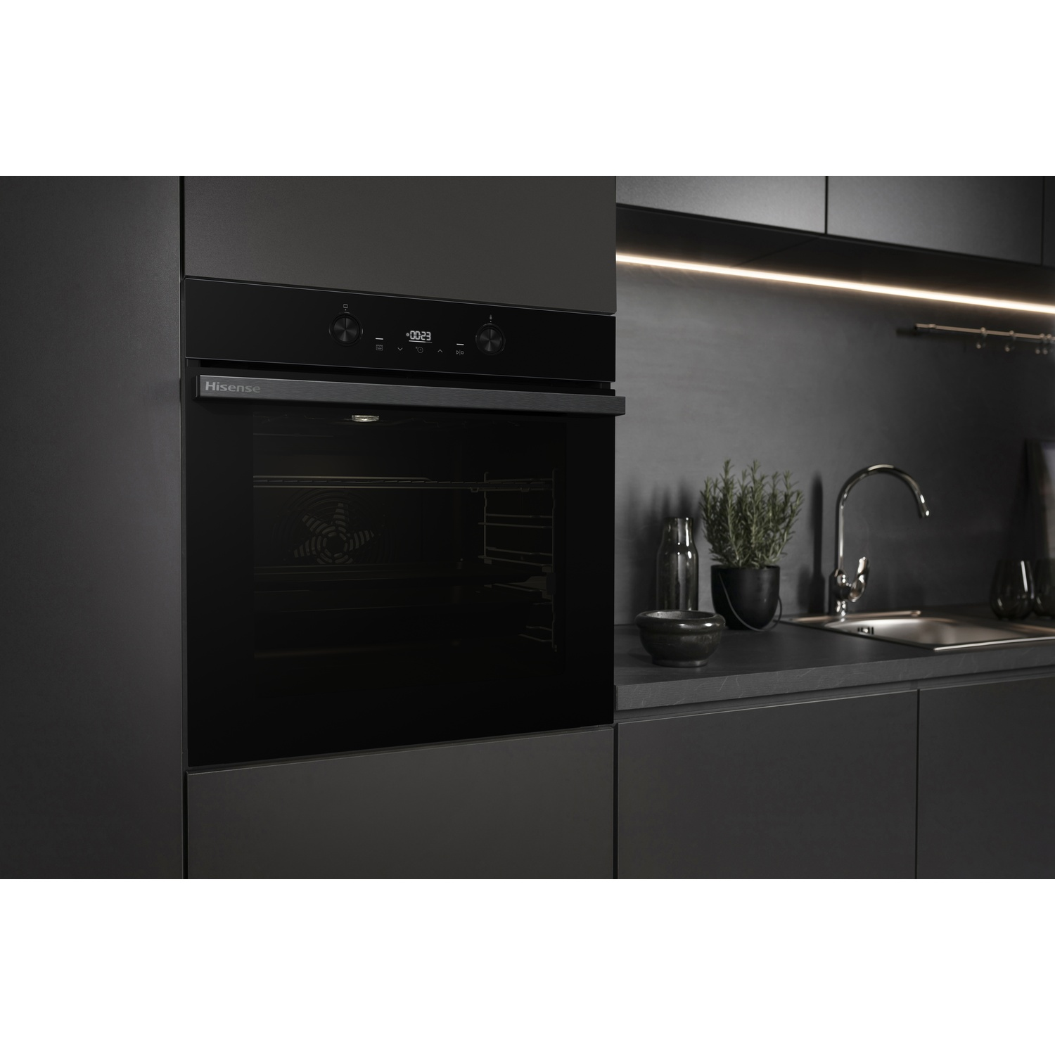 Un forno nero Hisense in una cucina moderna. Sono visibili un lavandino, piante e piani di lavoro. Il forno mostra un display digitale.