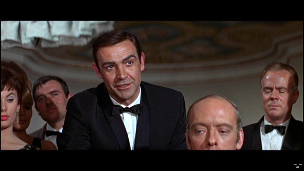 Sean Connery im Smoking, umgeben von Leuten in formeller Umgebung. Andere tragen Fliegen und Abendkleider.