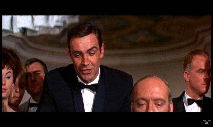 Sean Connery im Smoking spricht. Andere Personen in formeller Kleidung sind im Hintergrund. Innenaufnahme eines Raumes.