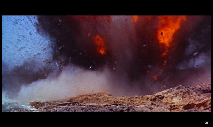 Eine Explosion mit Feuer und Trümmern. Eine große Rauchwolke steigt vor blauem Himmel auf. Der Vordergrund ist braun.