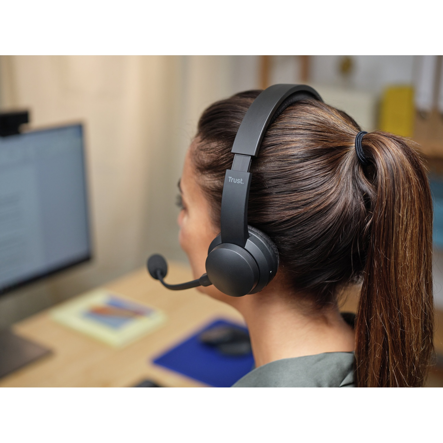 Una donna con cuffie nere e microfono. È seduta davanti a un computer, di spalle alla fotocamera.
