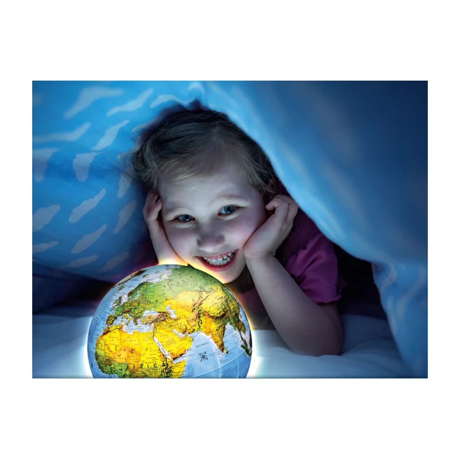 Una ragazza sorride, guardando un mappamondo illuminato sotto una coperta blu. Il mappamondo mostra i continenti. È dentro, illuminata dal mappamondo.