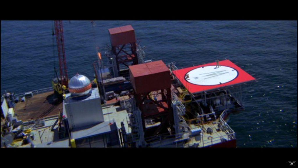 Luftaufnahme eines Schiffs mit rotem Landeplatz, zwei roten Strukturen, einem Kran und einer Metallkugel. Das Schiff befindet sich auf dem Meer.
