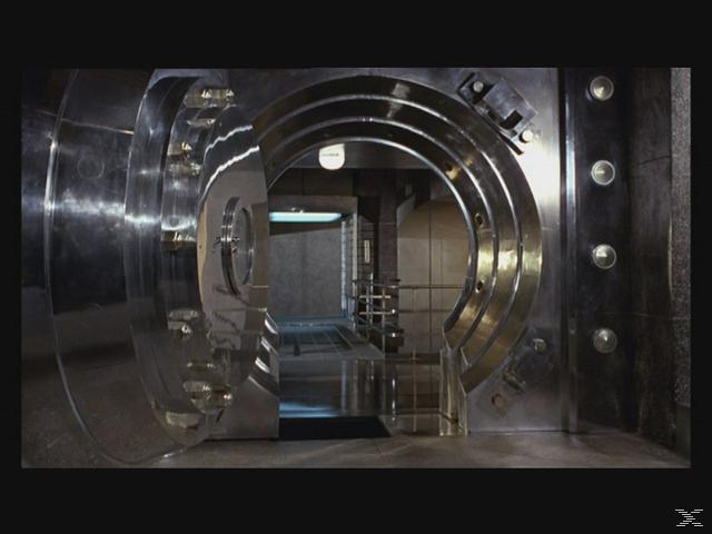 Eine große, offene Banktresortür zeigt einen Flur. Die Tür ist metallisch mit kreisförmigen Akzenten. Flur hat Metalltreppen und ein Licht.