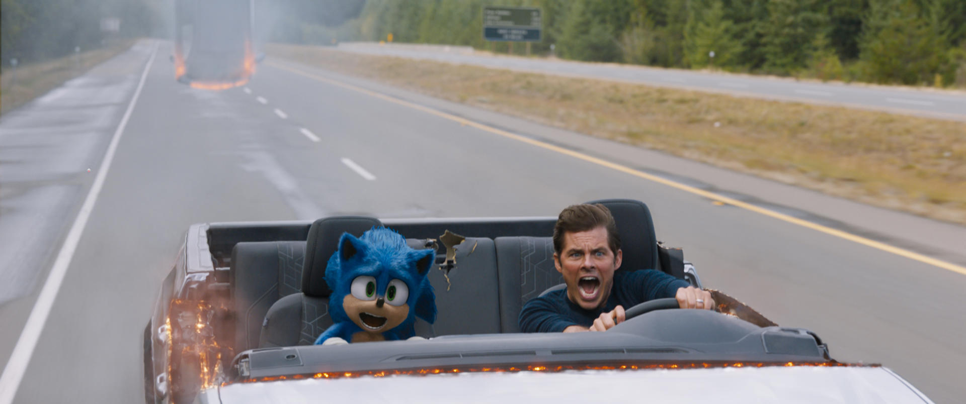 Sonic und ein Mann in einem Auto auf einer Autobahn. Ein weiteres brennendes Fahrzeug ist in der Ferne. Der Mann schreit.