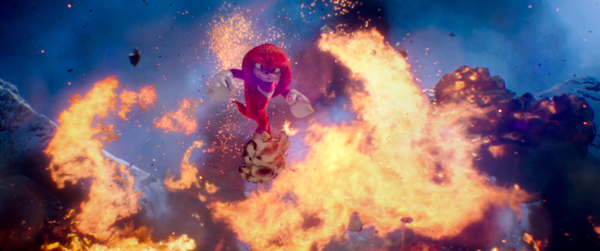 Roter Knuckles-Charakter inmitten von Explosionen. Feuer und Trümmer im Vordergrund, Berge und blauer Himmel im Hintergrund.