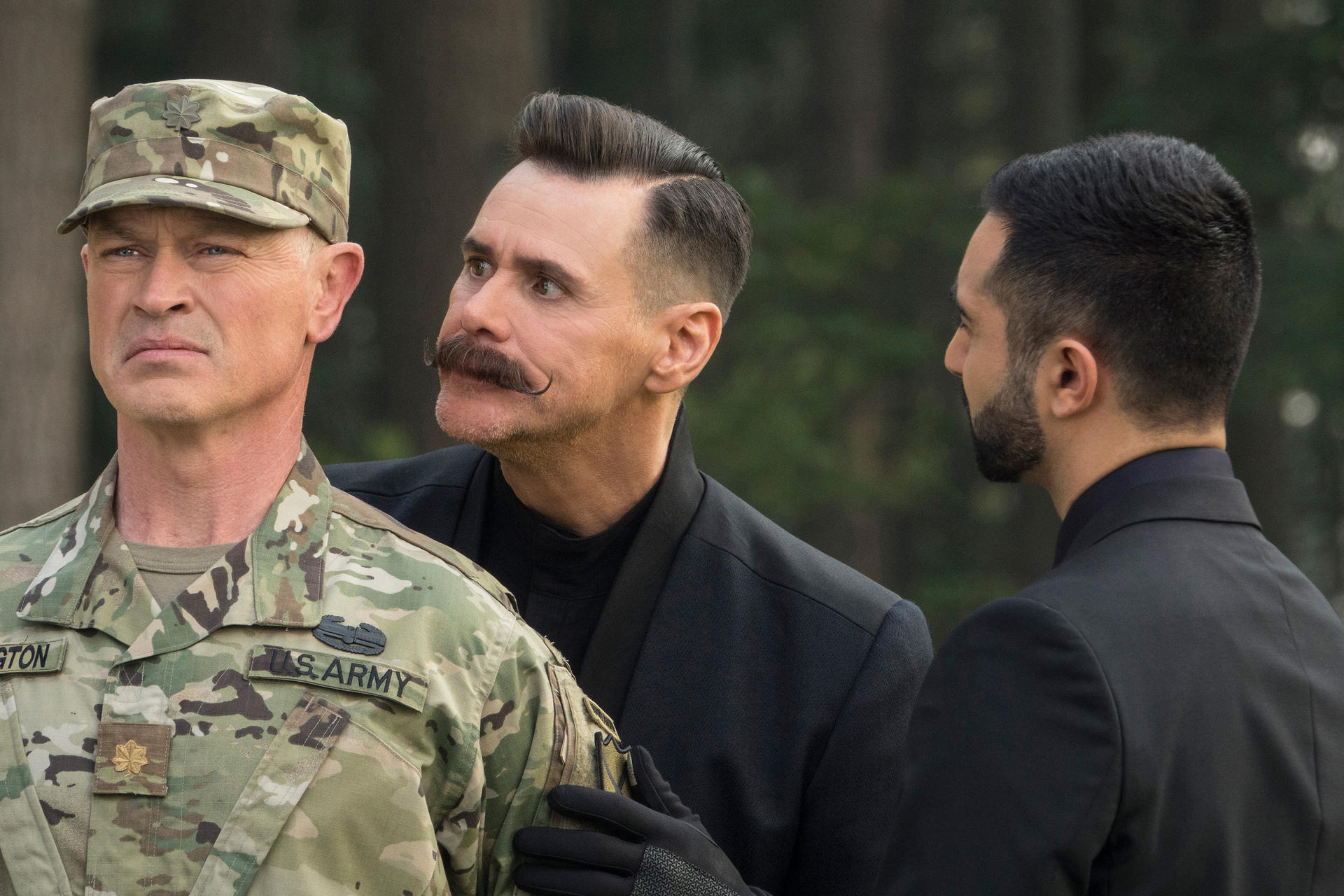 Drei Männer im Bild. Ein Soldat in Uniform, ein Mann mit Schnurrbart und ein weiterer Mann in einem schwarzen Anzug, die alle in verschiedene Richtungen blicken.