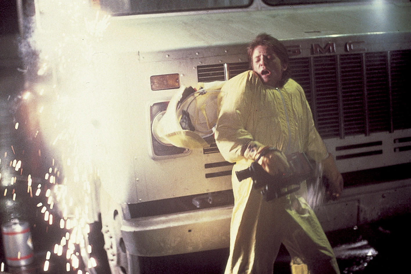 Mann in gelbem Anzug schreit in der Nähe eines Busses. Funken fliegen. Ein Gerät wird in der Hand gehalten. Ein Helm ist sichtbar.