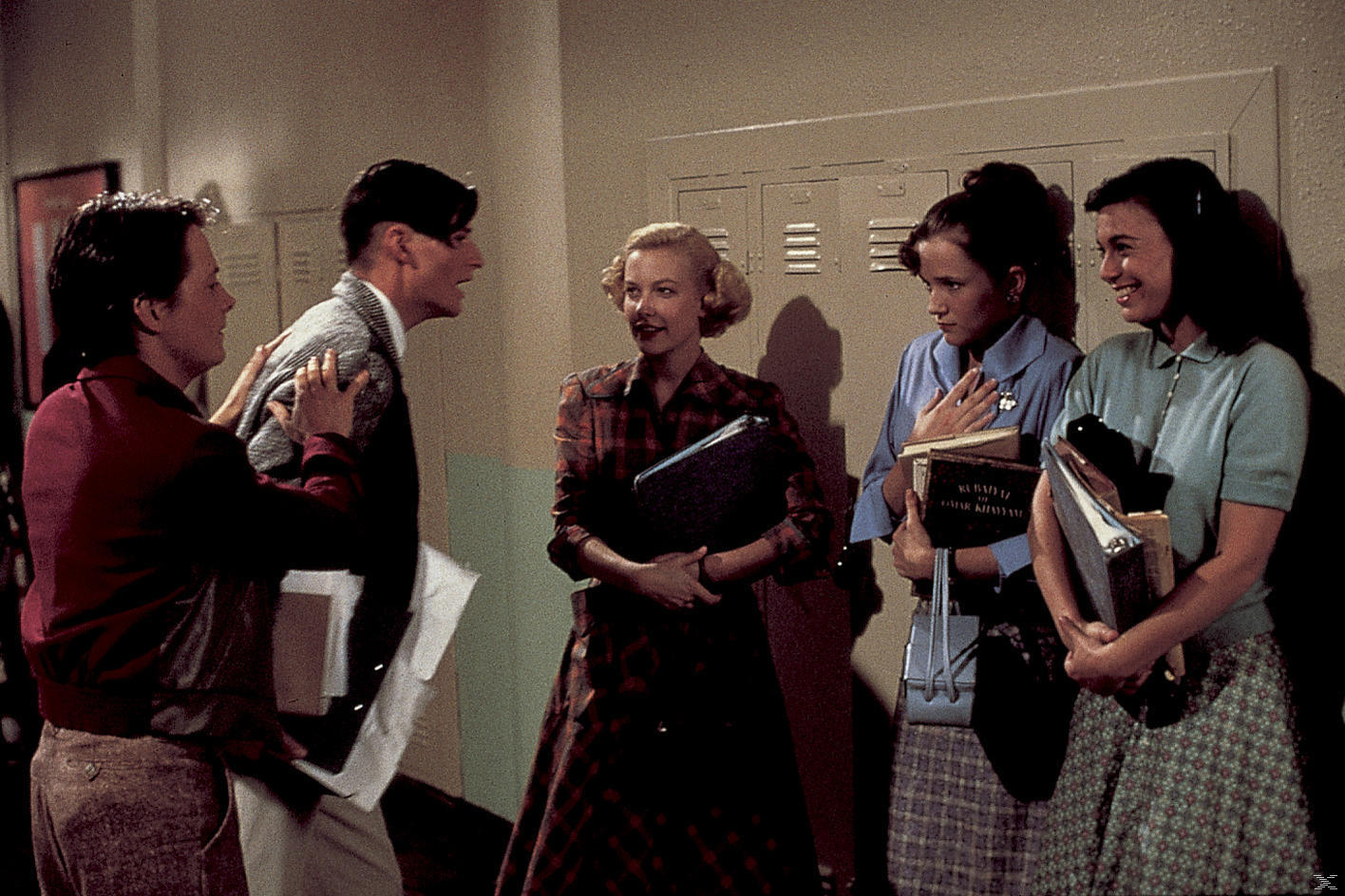 Eine Gruppe von Leuten in einem Schulflur. Ein Mann wird von einem anderen gehalten. Frauen halten Bücher.