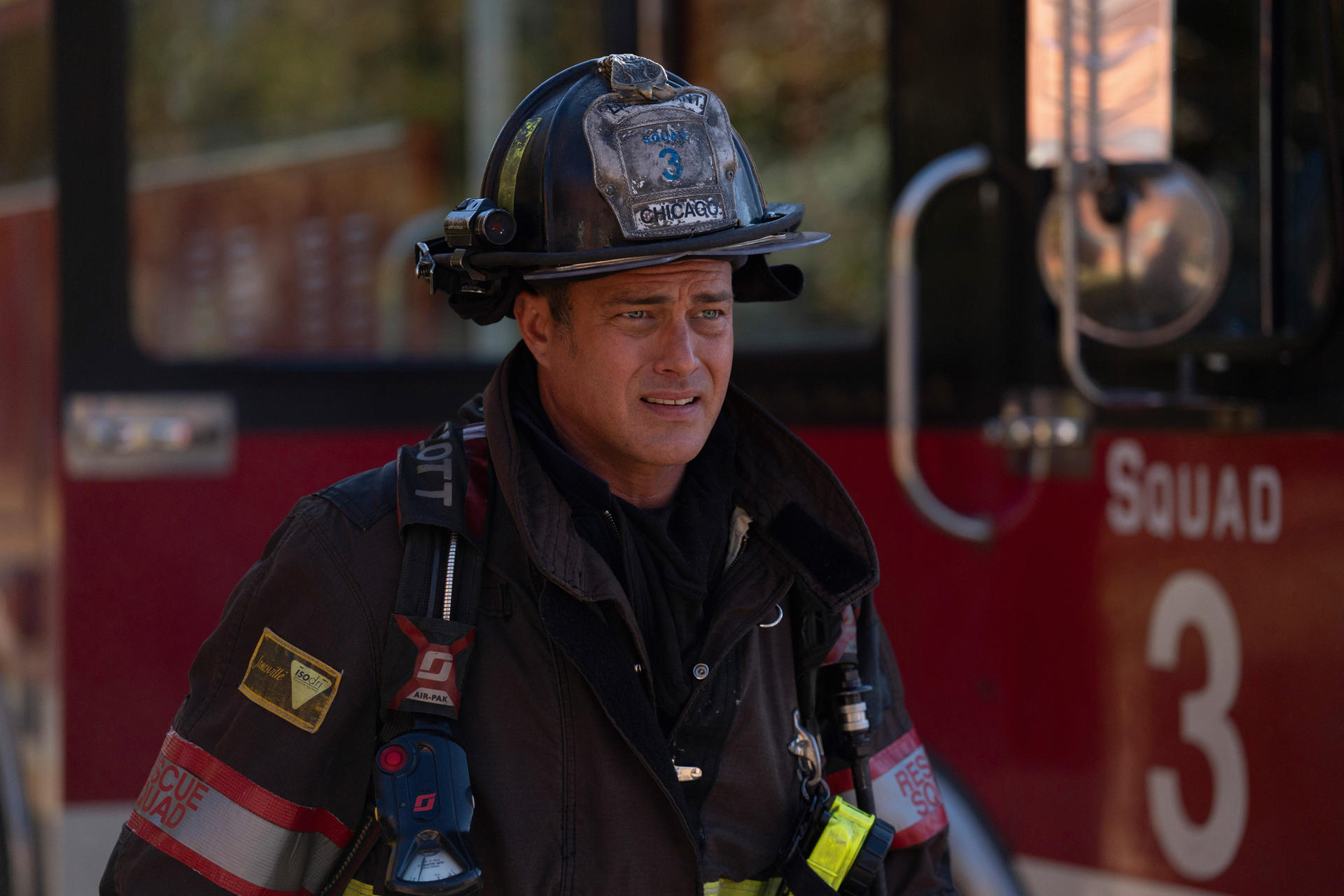 Ein Feuerwehrmann mit Helm steht vor einem roten Feuerwehrauto. Er trägt eine Uniform mit dem Schriftzug 'Rescue Squad'.