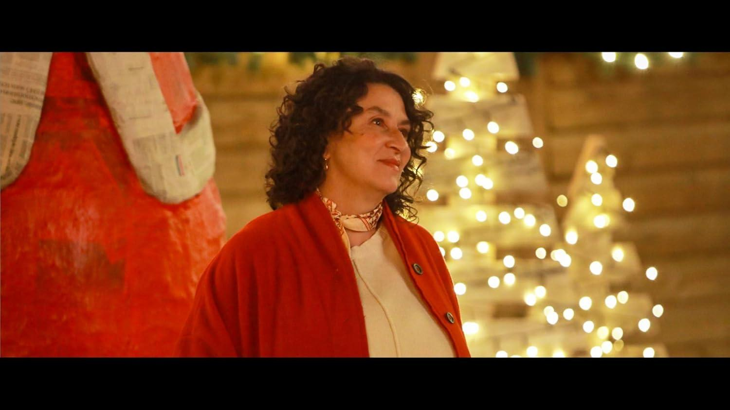 Frau im roten Mantel lächelt, vor dem Hintergrund von Weihnachtslichtern und einer roten Figur.
