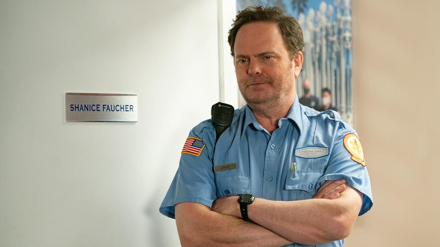 Mann in blauer Uniform mit verschränkten Armen. US-Flaggen-Aufnäher auf der Schulter. Namensschild 'Gray'. Schild mit 'Shanice Faucher'.