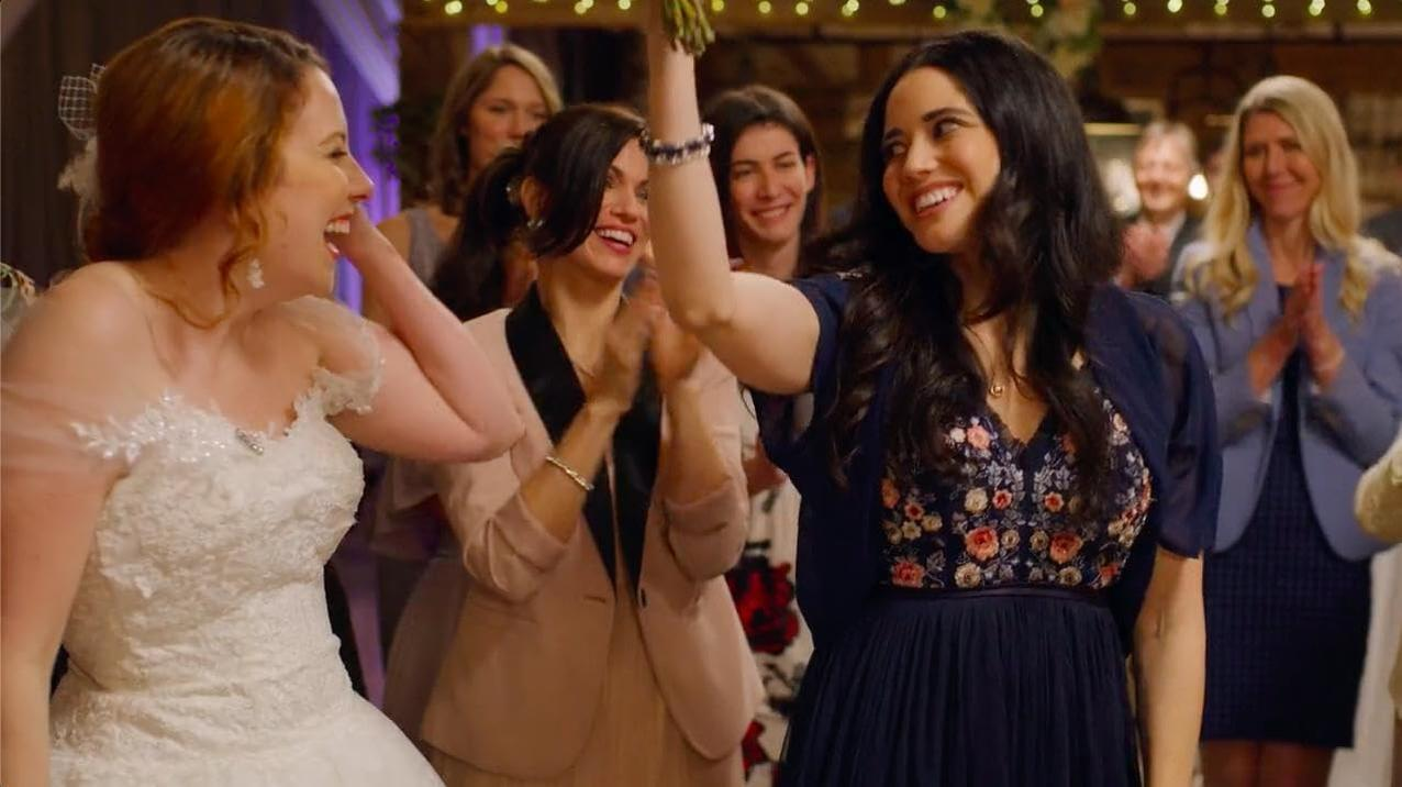 Frauen feiern bei einer Hochzeit, Braut im weißen Kleid. Andere klatschen und lächeln. Blumenkleid und Blazer vorhanden.