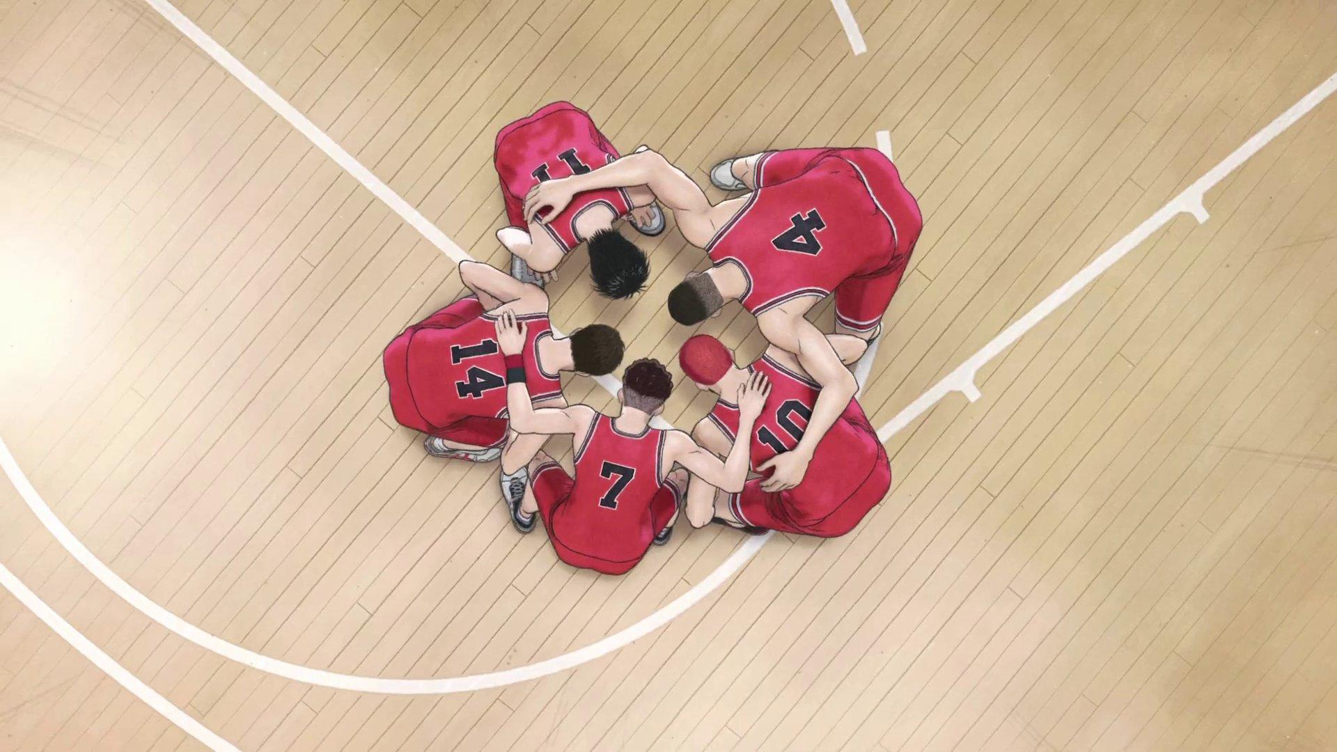 Ein Basketballteam versammelt sich auf dem Spielfeld. Die Spieler tragen rote Trikots mit weißen Nummern. Der Boden ist aus Holz mit weißen Linien.