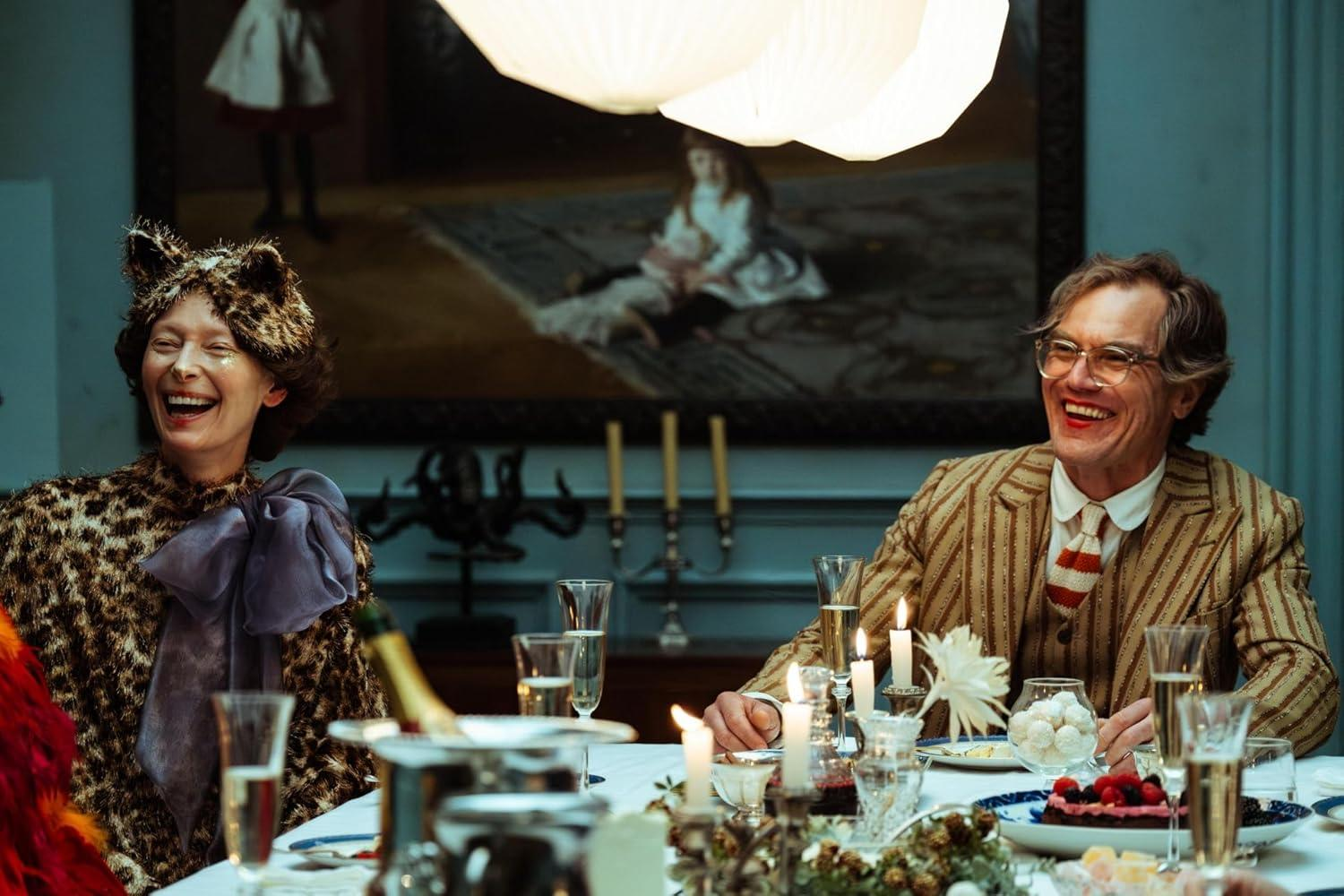 Zwei Personen lachen bei einem Abendessen bei Kerzenschein. Eine trägt ein Leopardenmuster-Outfit und Katzenohren, die andere einen Anzug und eine Brille.