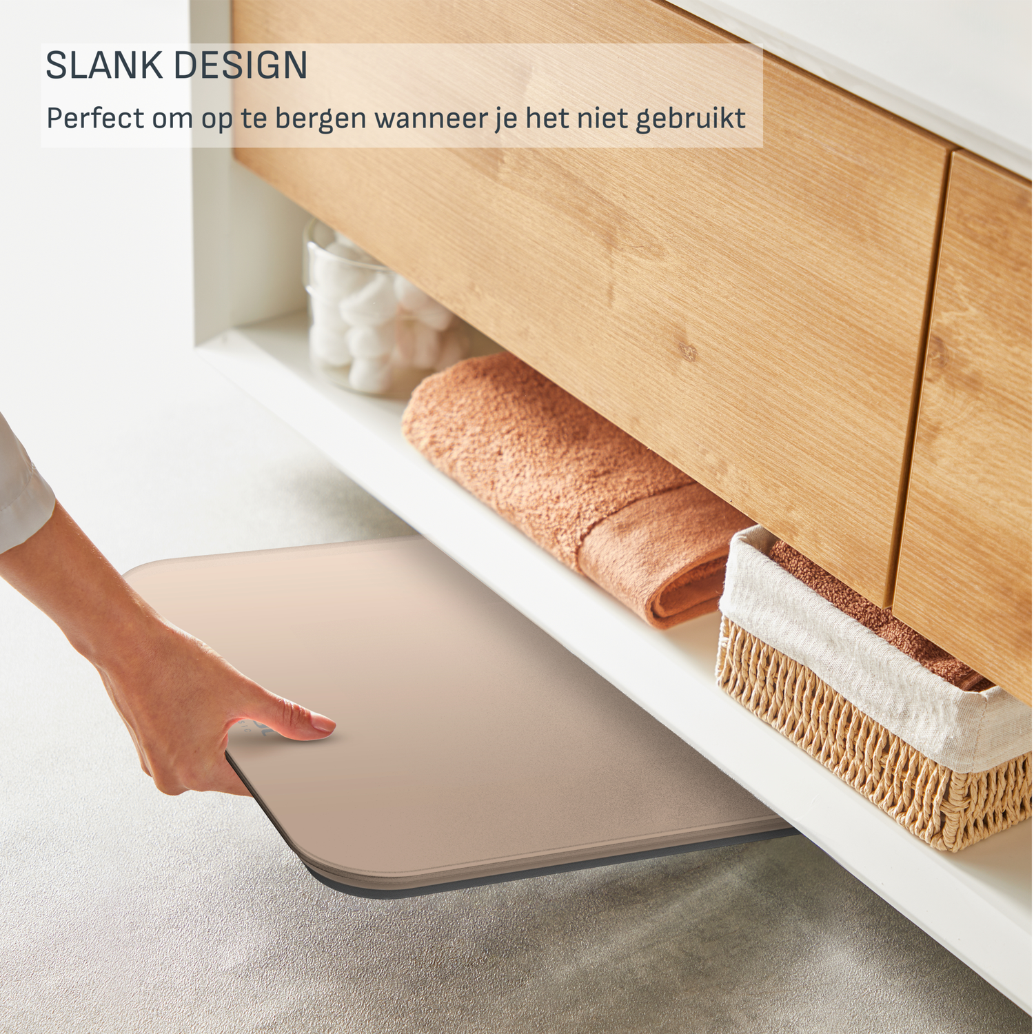 A hand pulls a mat from under a wooden cabinet shelf. Other items include a towel and a basket.