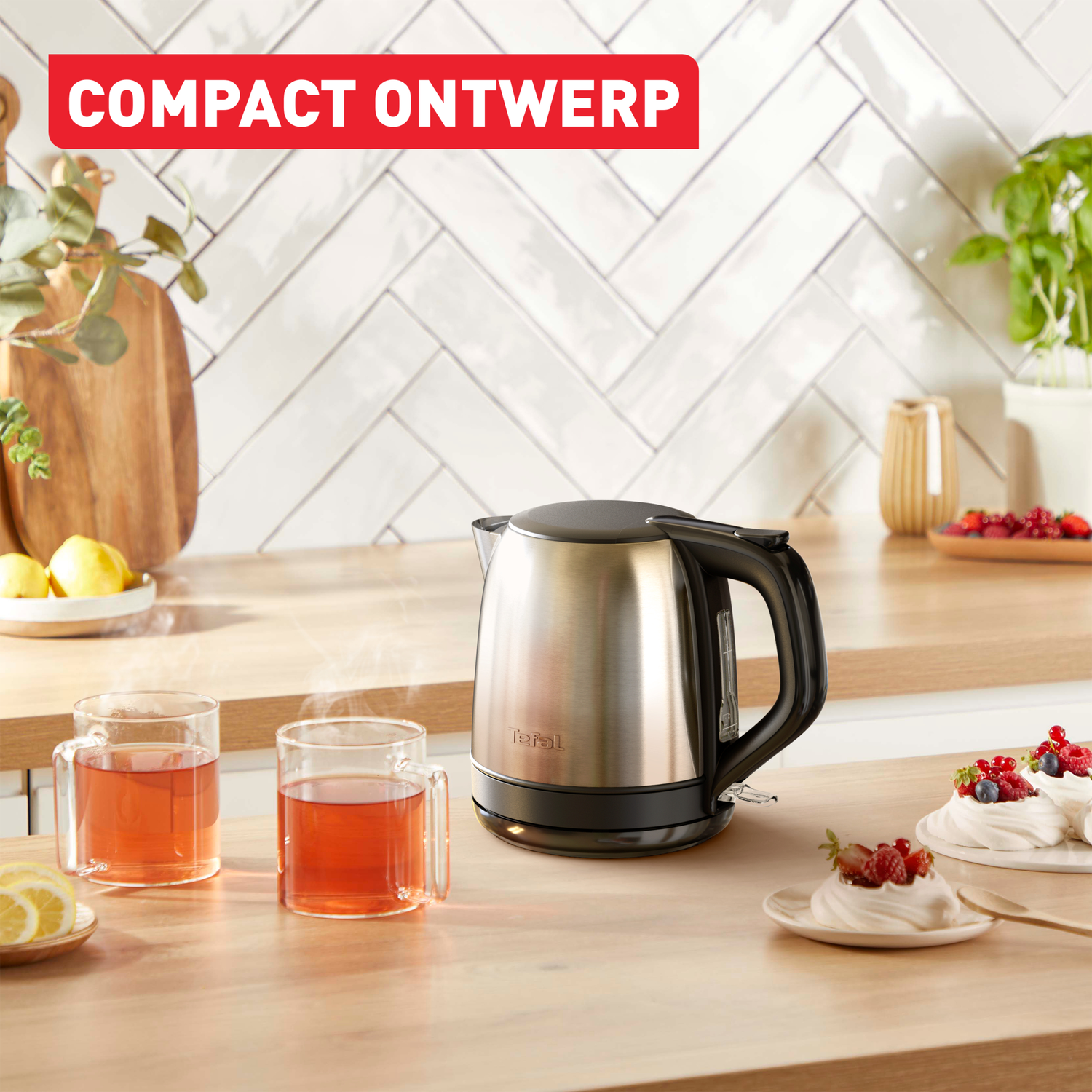 A kettle and two glass mugs with tea on a wooden countertop. Slices of lemon and desserts are also present.