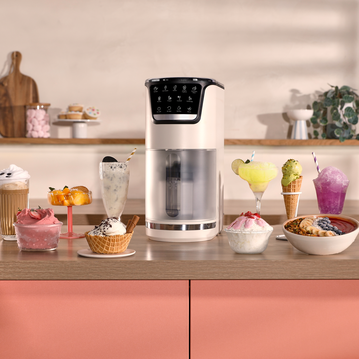 Een blender staat op een aanrecht met diverse drankjes en desserts. Een snijplank en planten staan op de achtergrond.