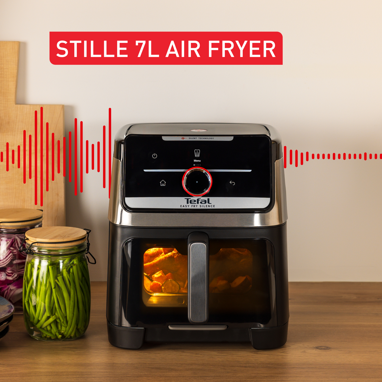 An air fryer with food inside, next to jars of pickled vegetables on a wooden surface. Text: Stille 7L Air Fryer.