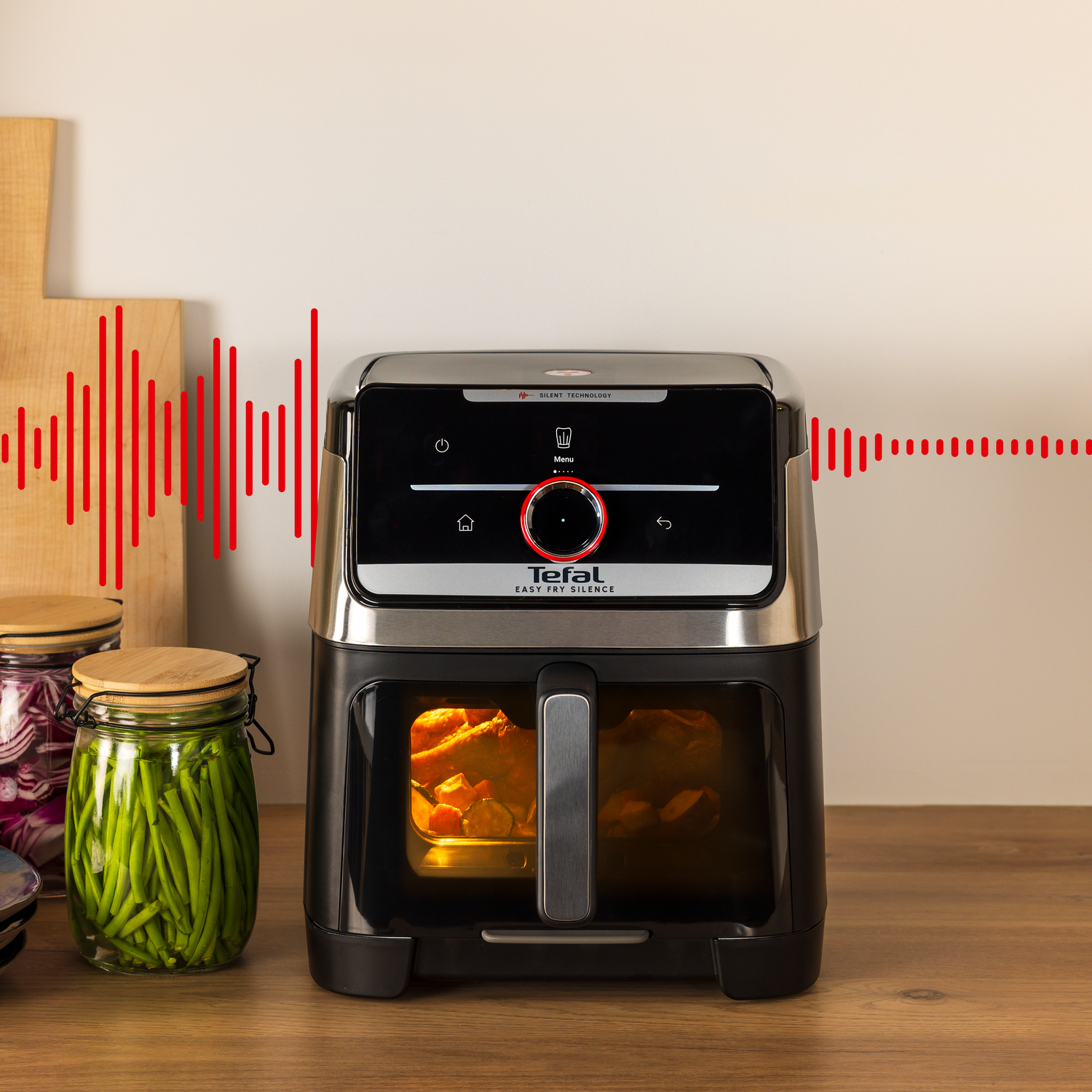 An air fryer with food inside. Jars of beans and onions sit nearby. Red sound waves emanate from the device.