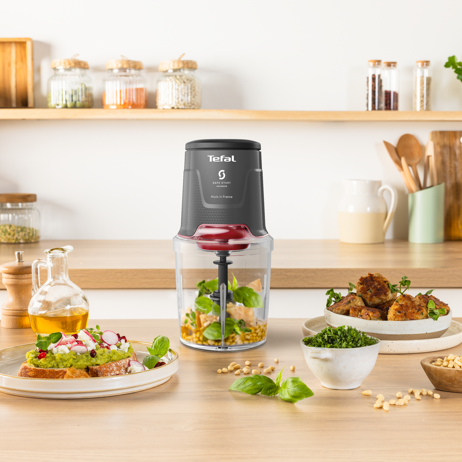 A kitchen scene features a food processor, pesto, appetizers, and ingredients on a wooden table.