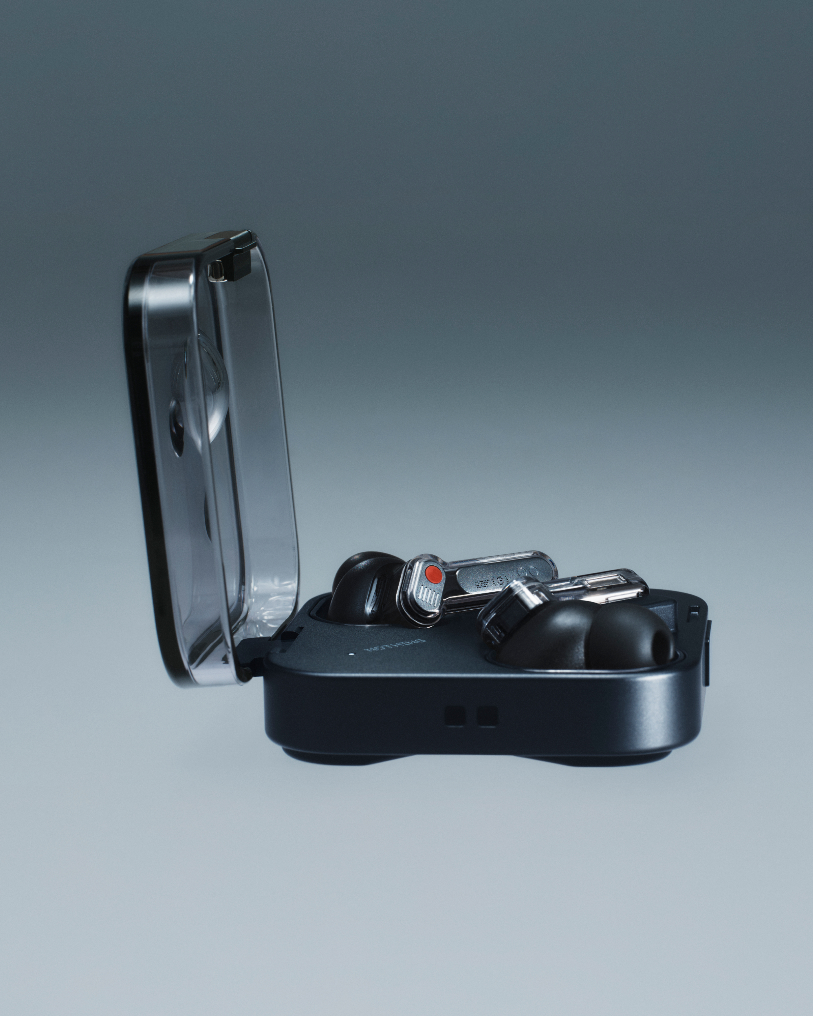 Ohrhörer in schwarzem Etui, Deckel offen. Ohrhörer sind schwarz mit rotem Punkt. Grauer Hintergrund.