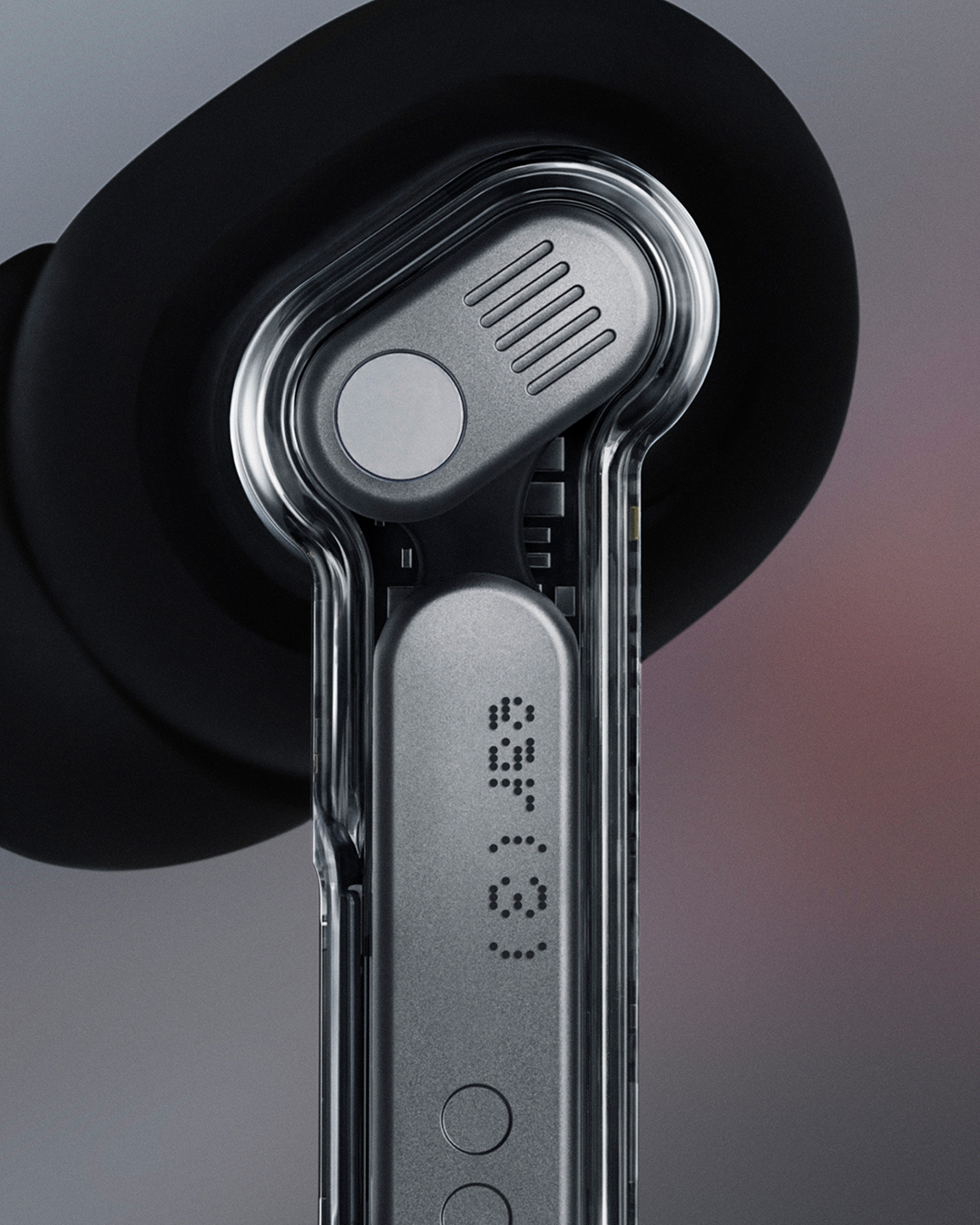 Nahaufnahme eines Ohrhörers. Er hat einen transparenten Kunststoffrahmen, einen grauen Metallkörper und eine schwarze Ohrspitze.