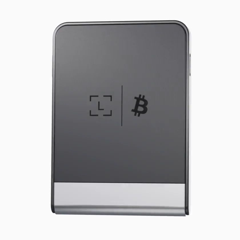 Egy téglalap alakú, sötétszürke eszköz ezüst alappal. Négyzet alakú logó és Bitcoin szimbólum található rajta.