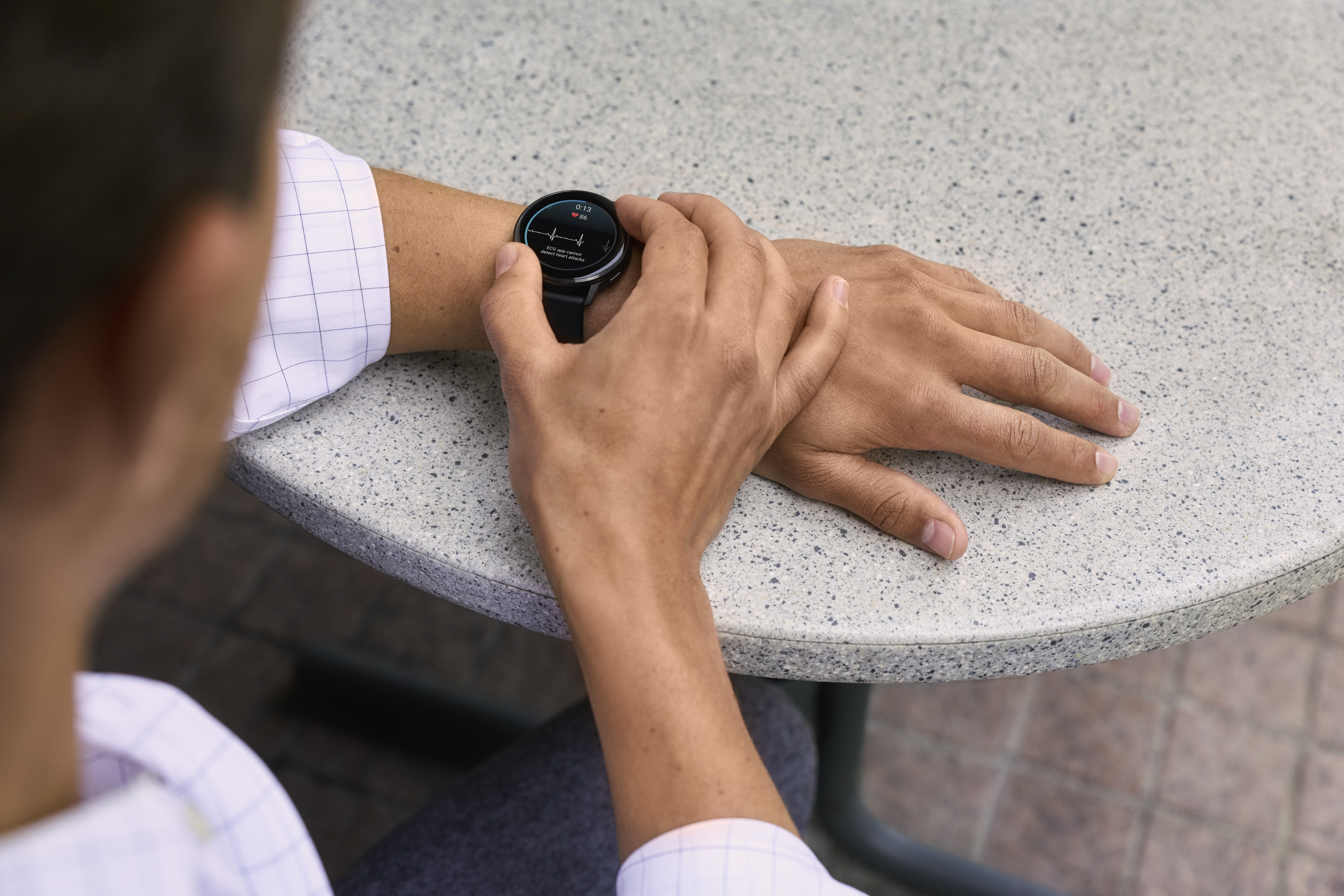 Eine Person, die eine Smartwatch trägt und ihren Puls misst. Die Uhr zeigt Daten auf einem grauen Tisch an.