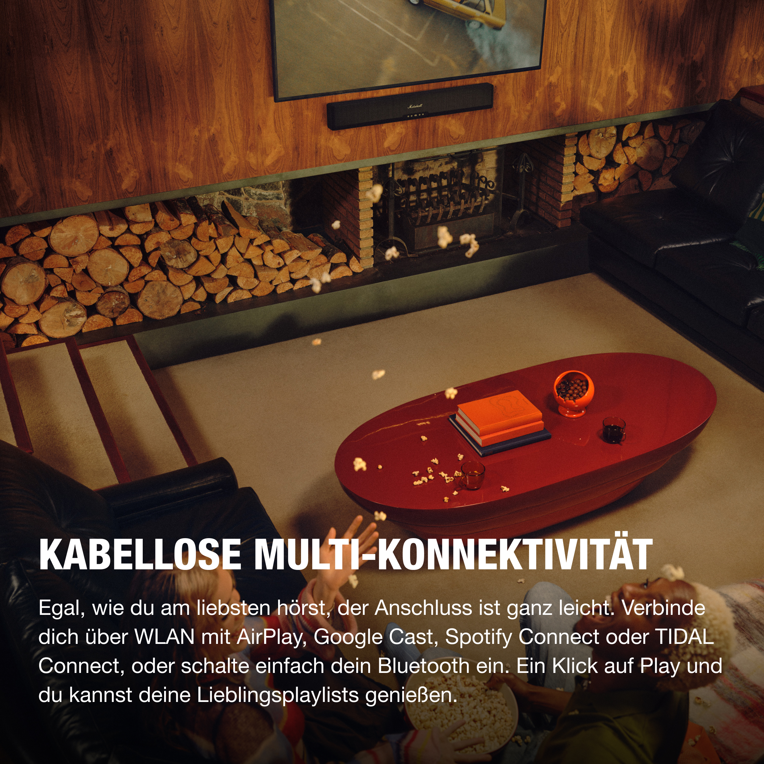 Ein Wohnzimmer mit rotem Tisch, Popcorn und schwarzem Sofa. Eine Soundbar ist an der Wand montiert.