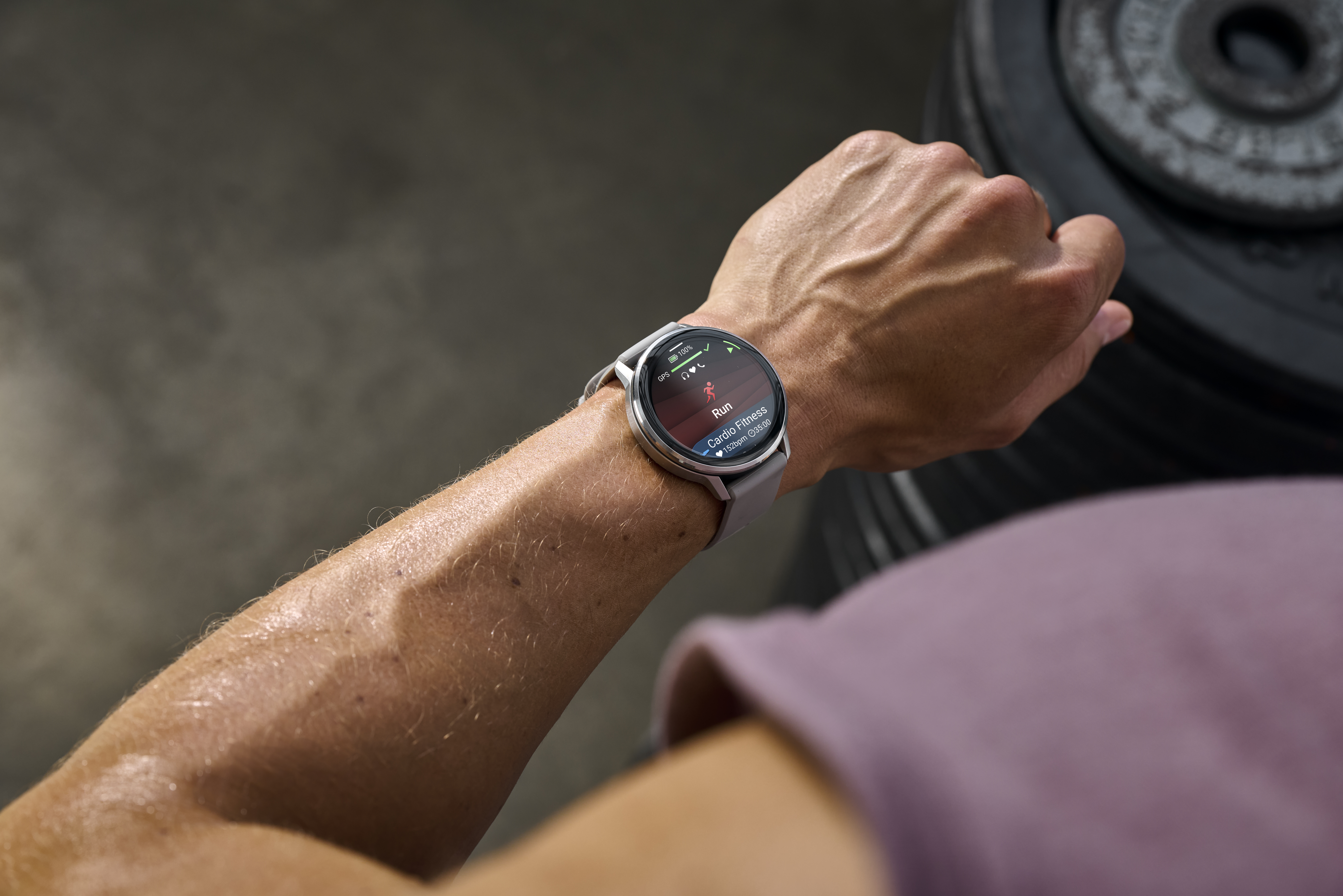 Arm eines Mannes mit Smartwatch, die ein Lauftraining anzeigt. Hintergrund sind Gewichte.